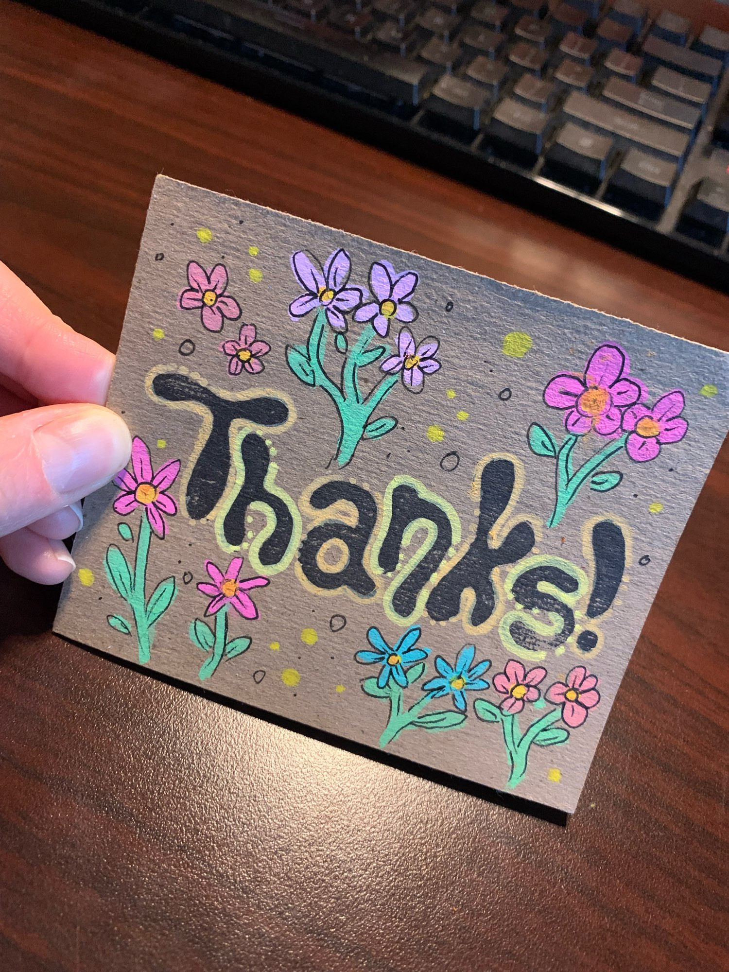 photo of a chipboard thank-you card hand-decorated with flowers in pinks and blues, in the middle is stamped the word "thanks!"