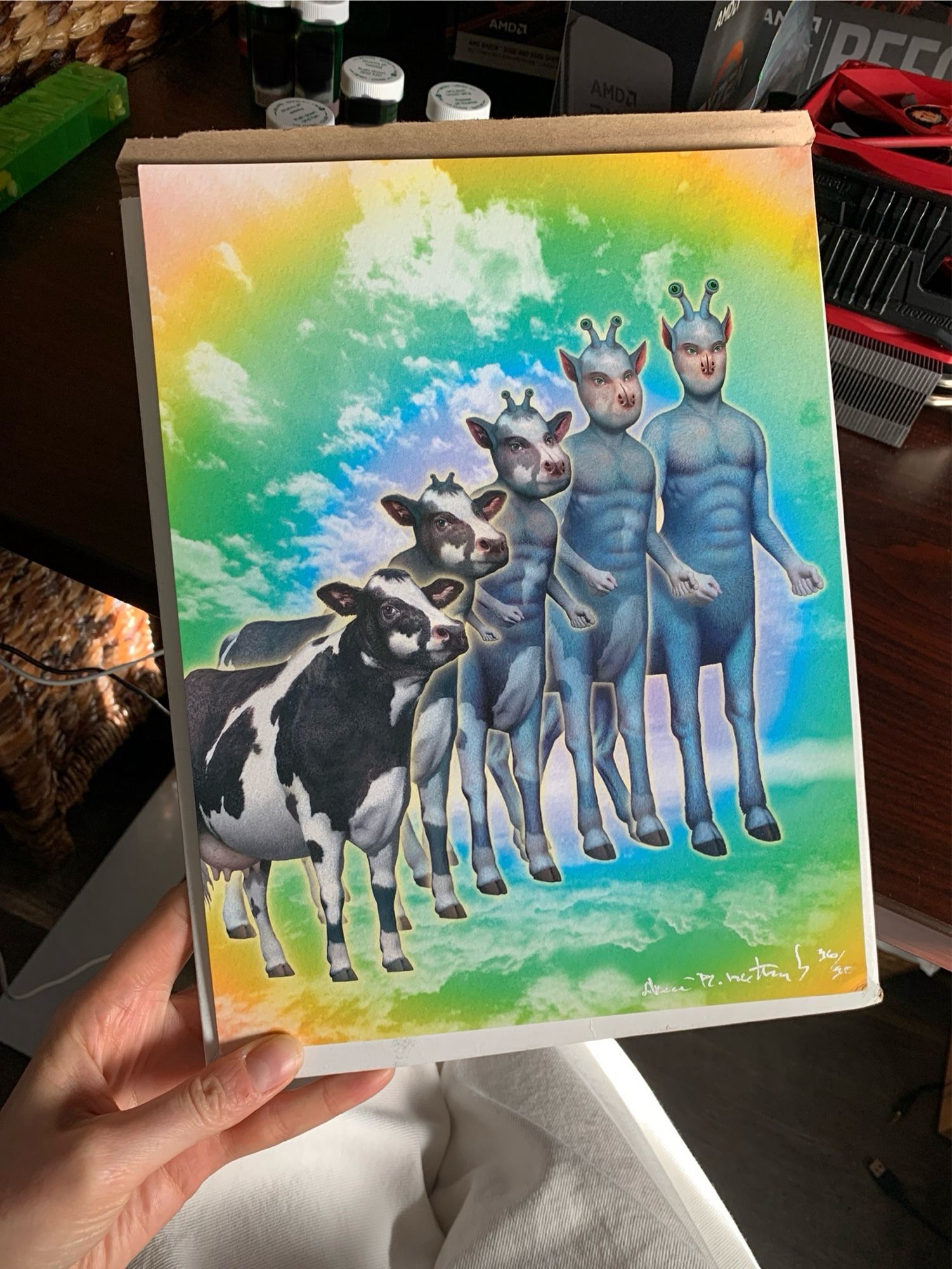 photo of me holding a signed print of an animorphs book cover in my hand. It is Ax the andalite (blue deer-scorpion centaur-looking alien with stalk eyes) morphing into a black and white moocow in front of a yellow, green & blue abstract cloudy backdrop.