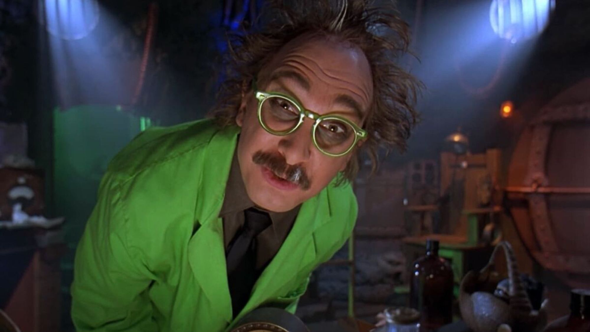 screengrab of what looks like probably MST3K The Movie, Dr. Forrester is a middle aged guy with wild brown hair with a white streak, bright green glasses, a brown mustache with a white streak and a bright green labcoat. He looks crazy and tired.