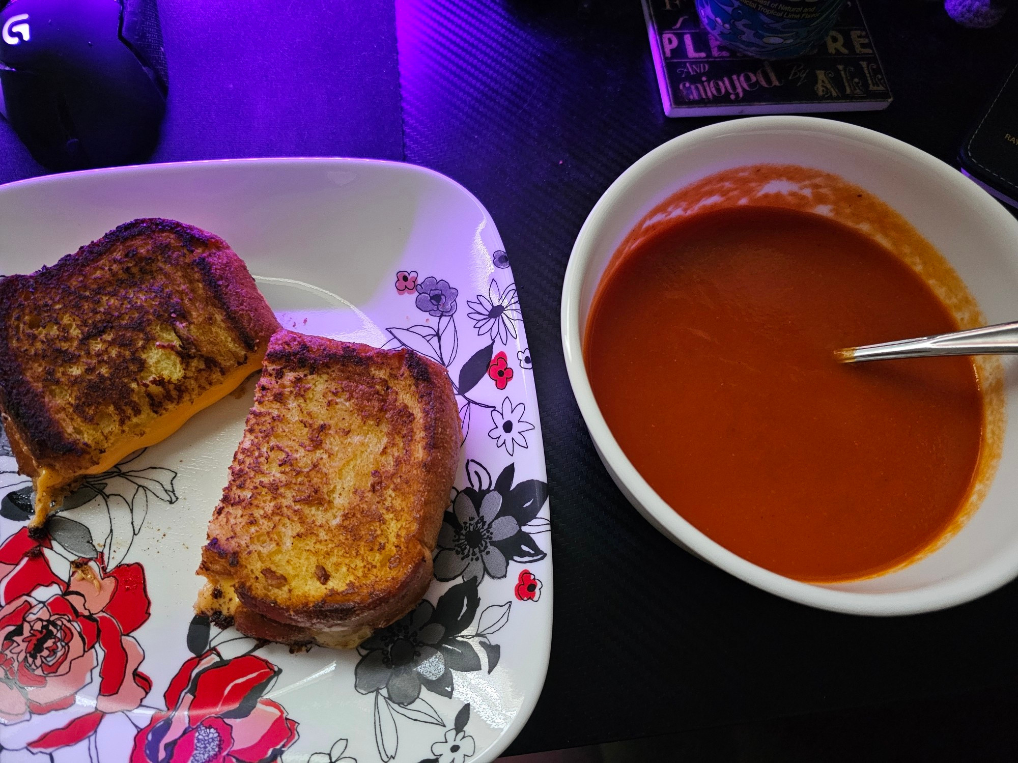 On the left, a grilled cheese rests atop a floral plate. It is perfectly grilled and cut in half.
On the right is a bowl of tomato soup, dangerous in its flavour profile.