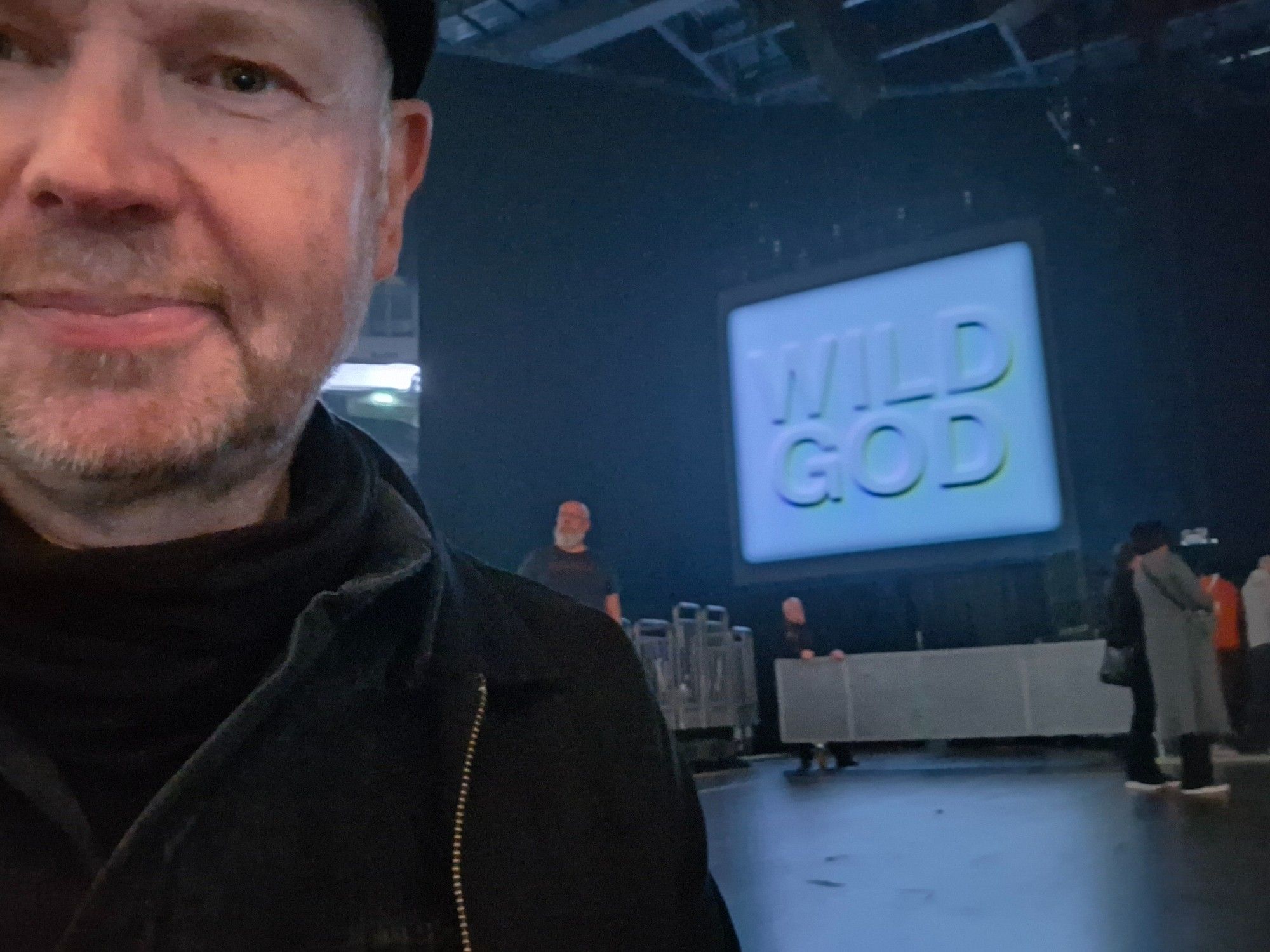 Ich vor der Bühne in der Uber Arena. Im Hintergrund ein großer Bildschirm mit der Aufschrift "Wild God"