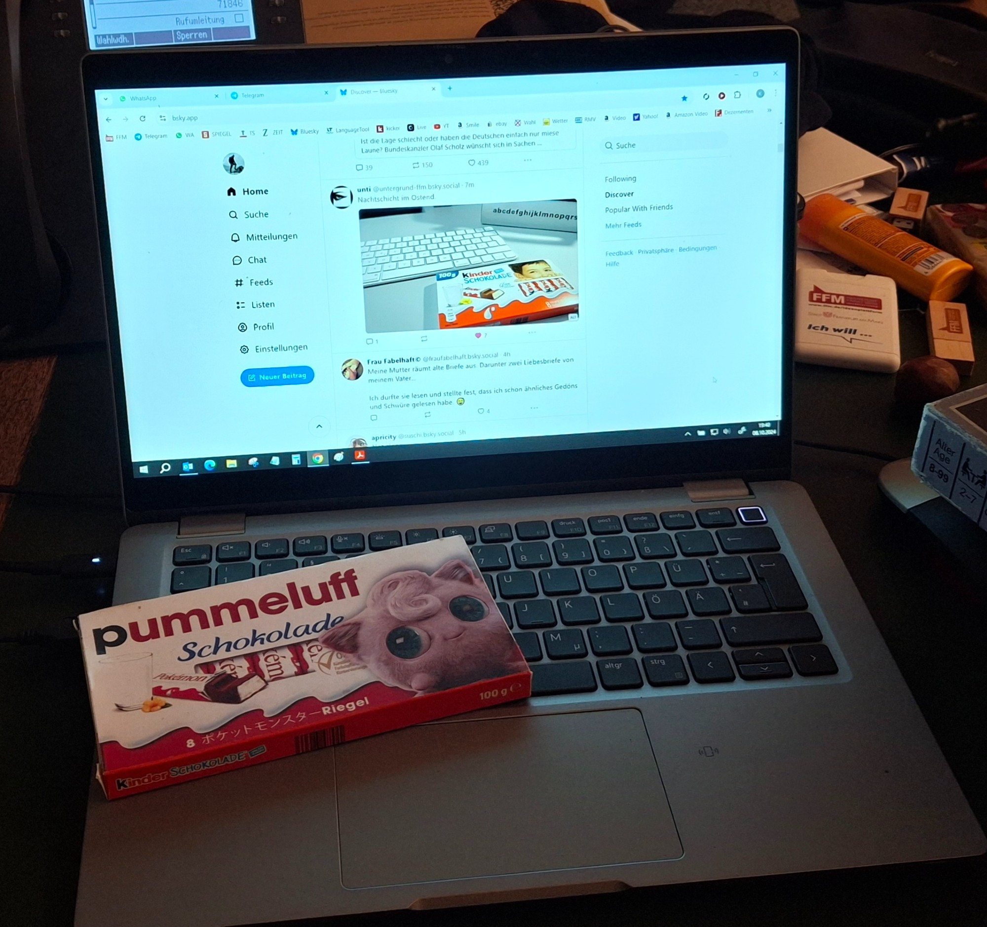 Eine Tafel kinderschokolade mit Pummeluff auf der Verpackung liegt auf der Tastatur eines Notebooks. Auf dem Display das Notebooks ein ähnliches Bild auf Bluesky zu sehen