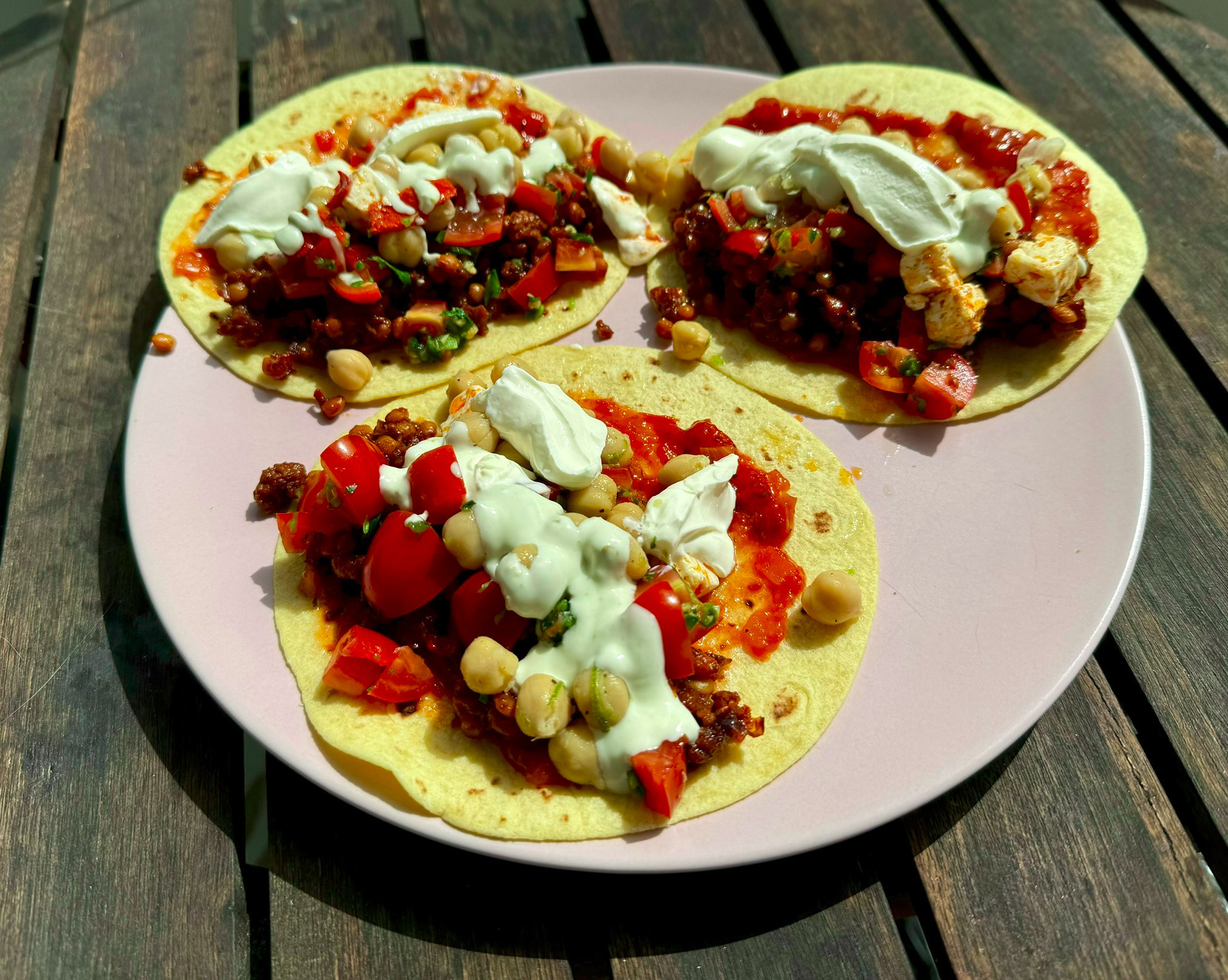 Tacos with chickpeas, tomatoes, red lentils and creme fraiche on a pink plate on a wooden table.