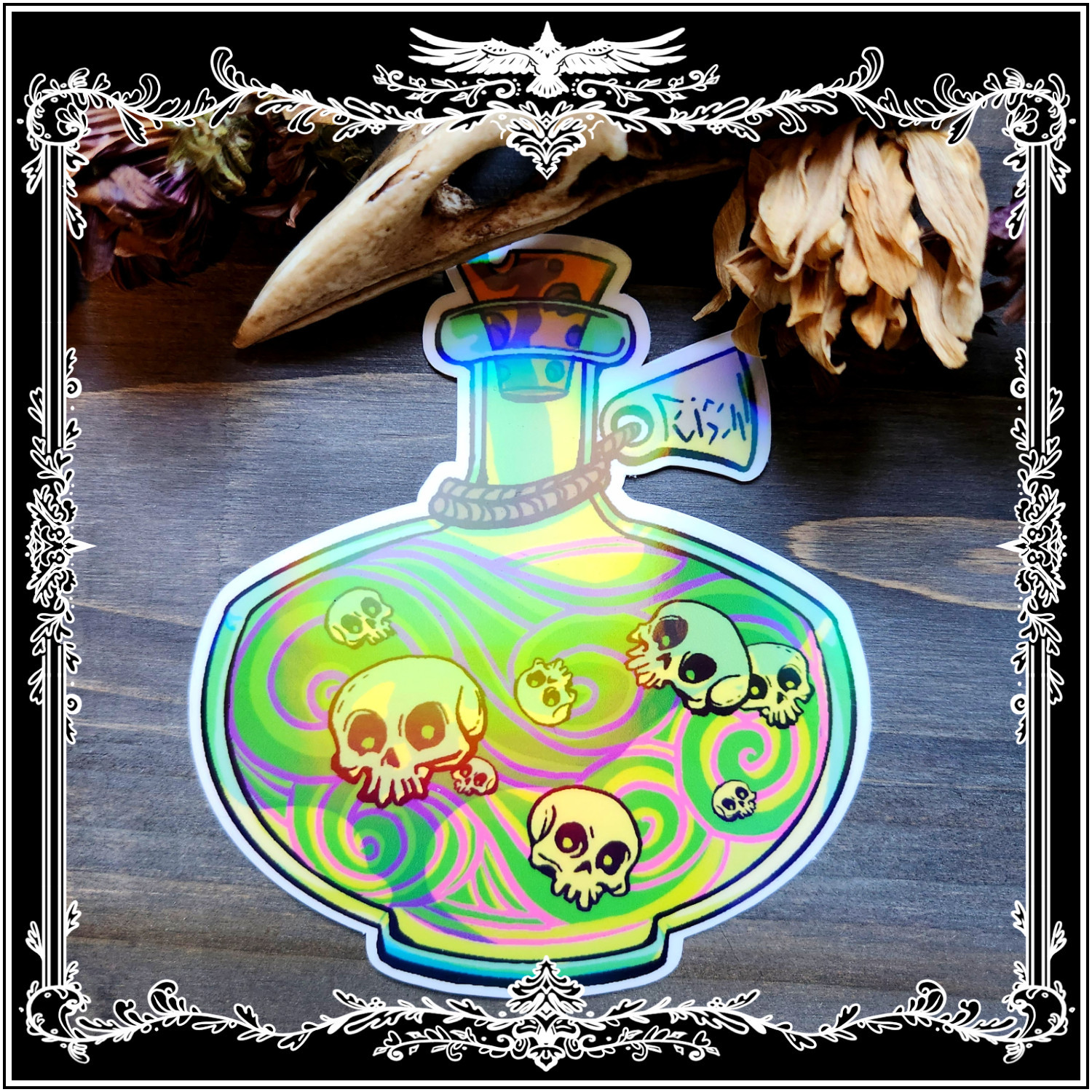 Poison Bottle
A picture of a die-cut vinyl sticker against a wooden background, framed with the beak of a raven skull and some dried flowers.
The sticker is a poison bottle full of a green liquid and small floating skulls. This particular version also features an AB holographic laminate that lends an “oil-slick” finish to the sticker.
The item (and its gloss variant) is for sale in my Etsy Shop CAdamsArt :)