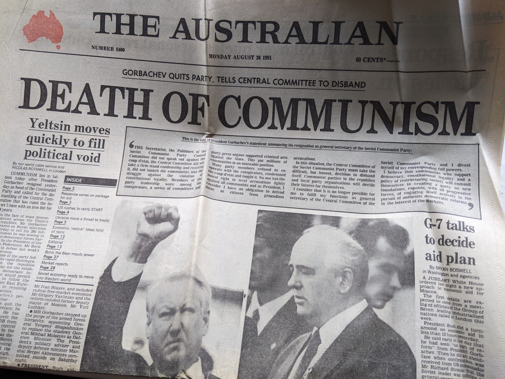 The front page of the newspaper The Australian from the 26th August, 1991. The large headline reads Death of Communism. The smaller headline above reads Gorbachev quits party, tells Central Committee to disband. The story headline reads Yeltsin moves quickly to fill political void. The two black and white photographs above the fold are: on the left, Boris Yeltsin stands with fist raised; on the right, Mikhail Gorbachev with downcast eyes (he's possibly reading a speech).