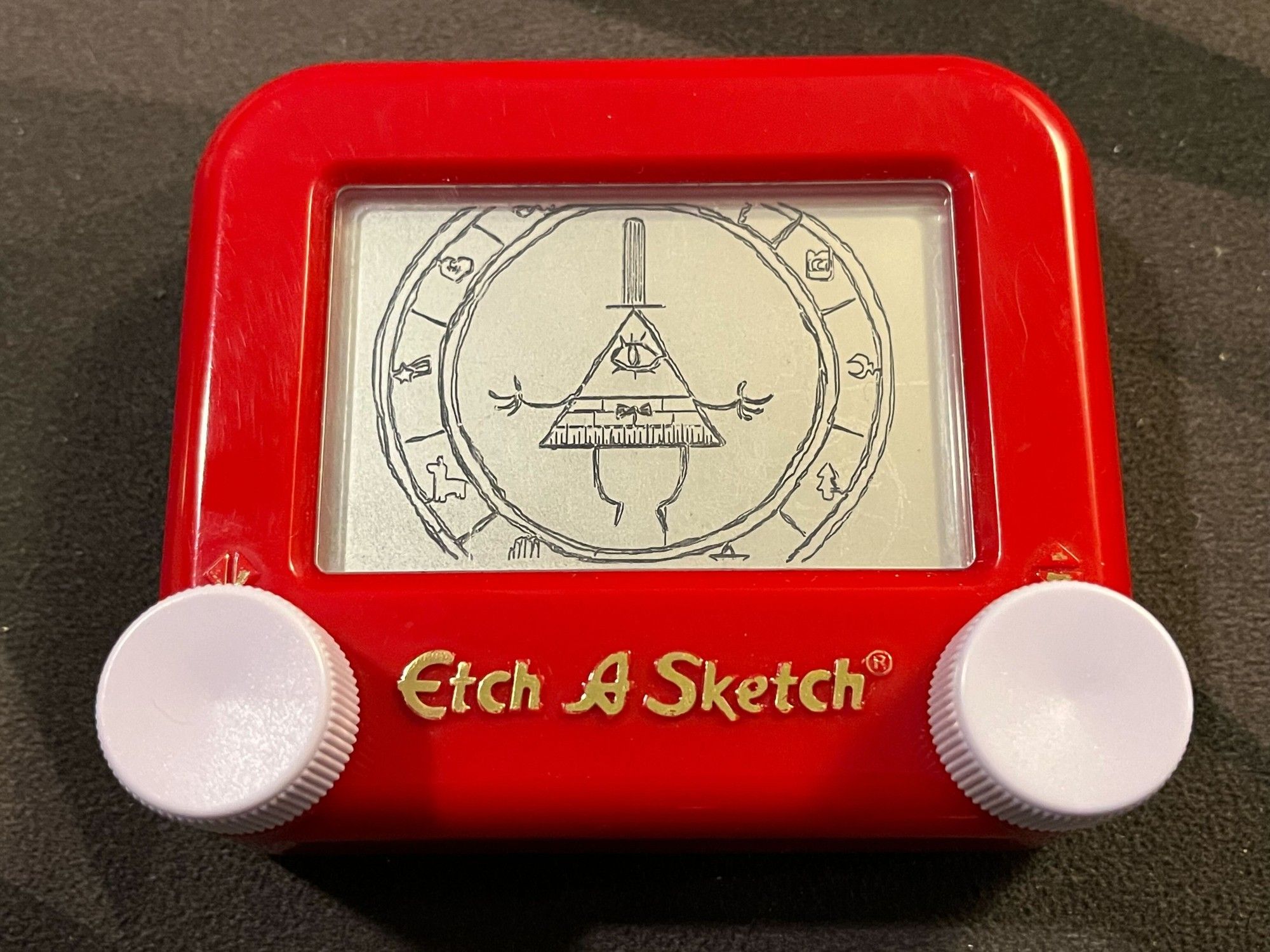 Pocket Etch-a-Sketch drawing of Bill Cipher from 'Gravity Falls' floating in the center of a ring with various little icons on it.