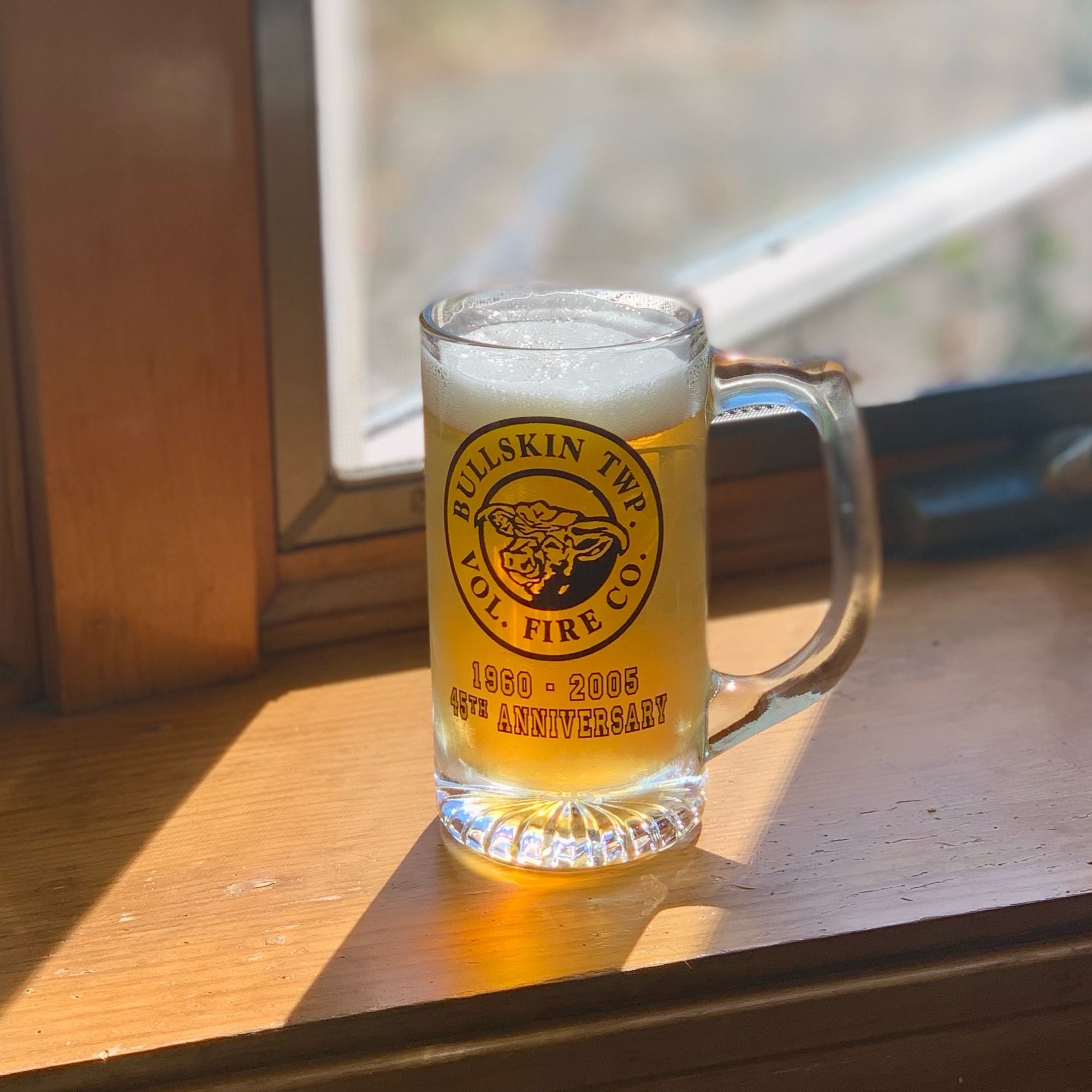 a glass stein from the bullskin township volunteer fire company’s 45th anniversary in 2005 filled with beer sitting on a sunny windowsill