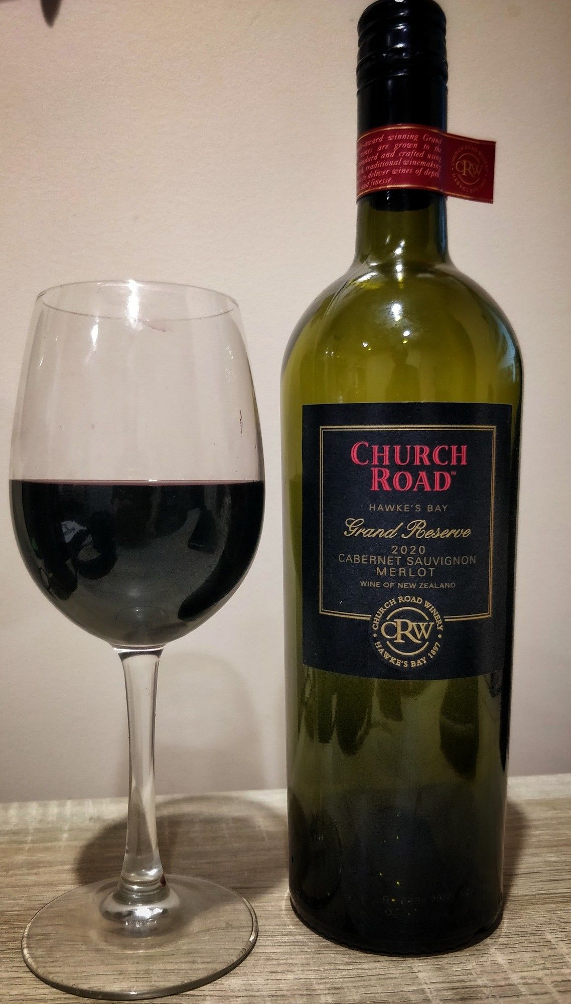 Glass of Church Road 2020 Grand Reserve Cab Merlot beside the empty bottle.