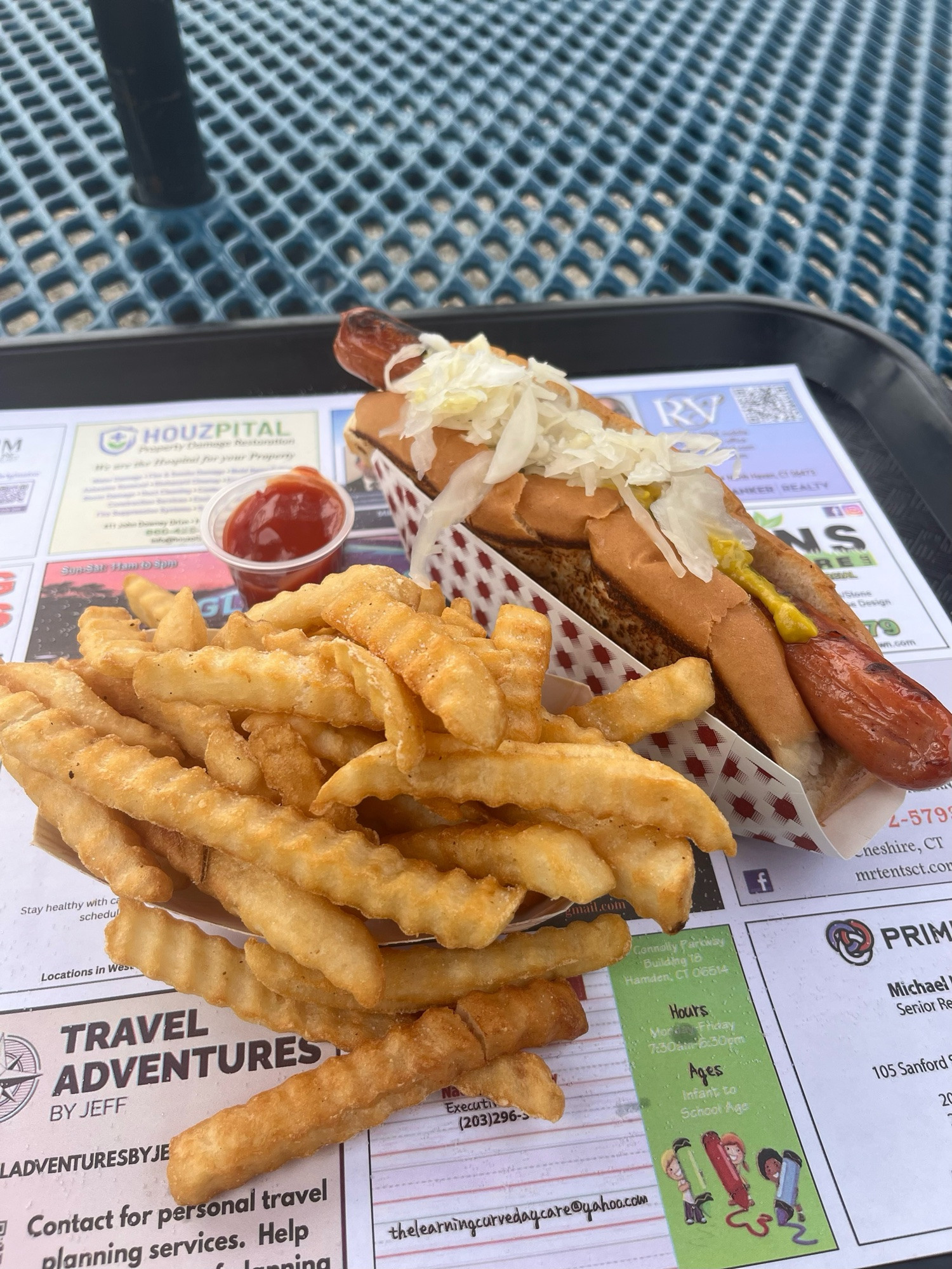 A tray holds a dish of crinkle cut, french fries and a hotdog with sauerkraut.