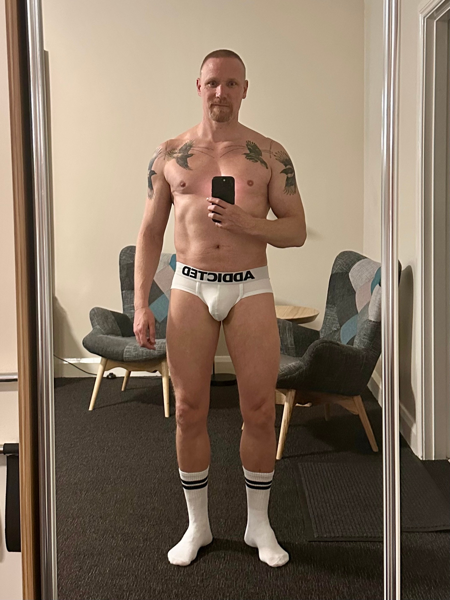 Full length mirror selfie of Timo. He’s wearing white Addicted briefs and white socks with two black stripes. 