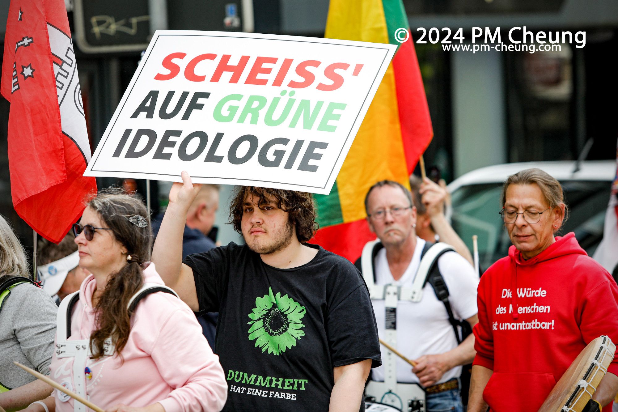 Auf diesem Bild führt ein Demonstrant ein Schild mit der Aufschrift "Scheiss' auf Grüne Ideologie". Der Demonstrant trägt dabei ein T-Shirt mit der Aufschrift "Dummheit hat eine Farbe".