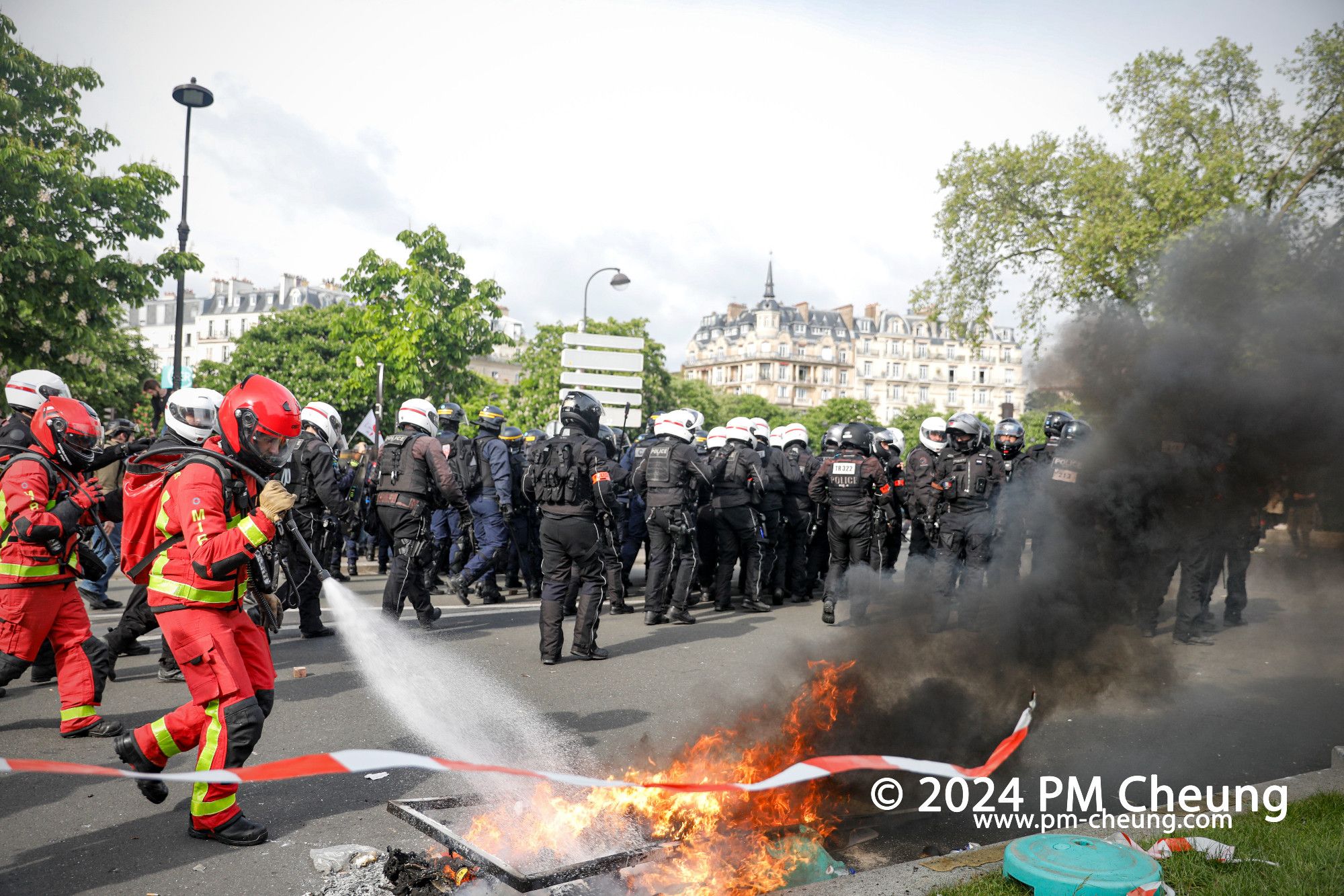 Auf dem Place de la Nation löscht die Feuerwehr einen kleinen Brand. Dahinter ist eine Gruppe von der „Brigade de répression de l'action violente motorisée (BRAV-M)“ zu sehen.