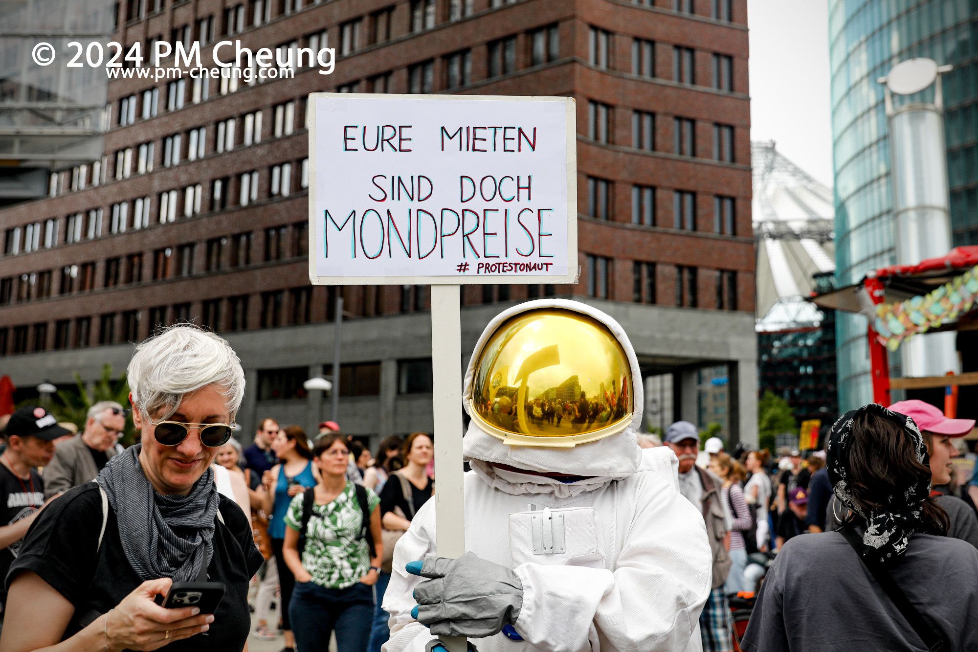 Am Potsdamer Platz hält ein - als Astronaut verkleideter - Demonstrant*in ein Schild mit der Aufschrift "Eure Mieten sind doch Mondpreise. #Protestnonaut".