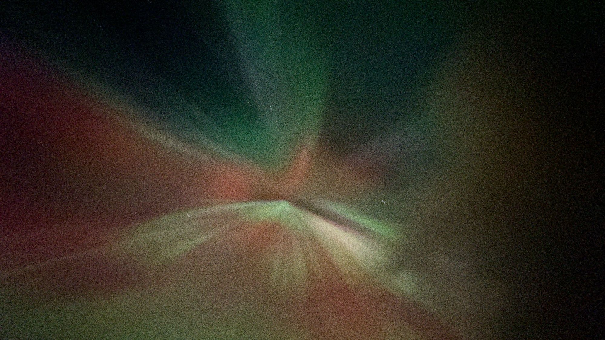 Photo of aurora spreading out from a central point, looking almost like a starburst. It has green and red bands of light.