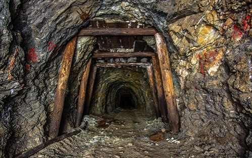 Dilapidated mine shaft, rocky gravel floor with rough walls and ceiling. The roof is held up with worm wooden beams