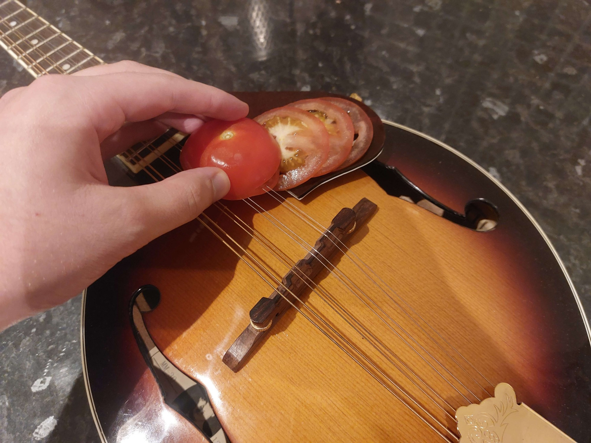 A photo showing what appears to be a tomato being cut by a mandolin (the musical instrument)