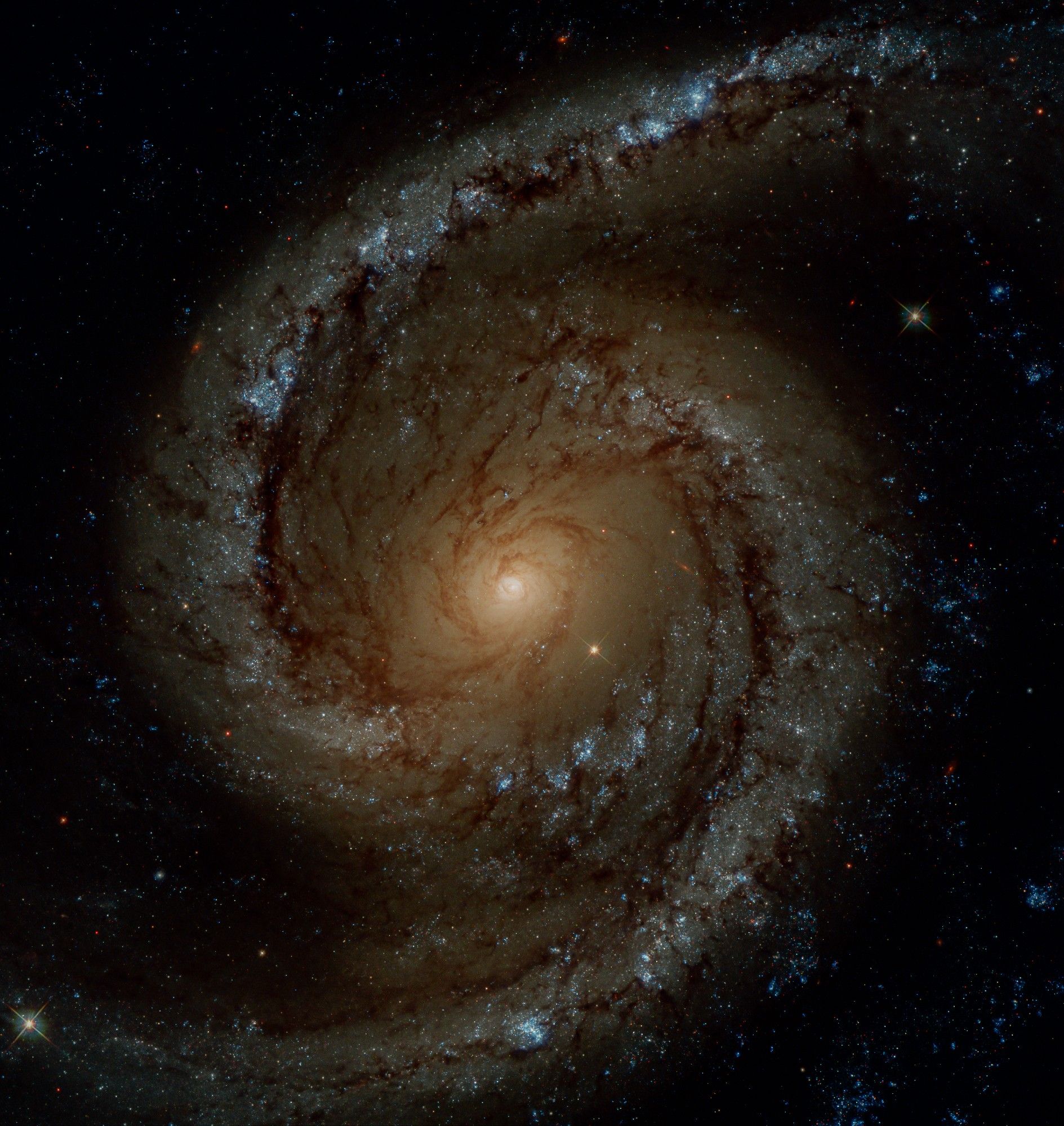 A spiral galaxy with a bright orange center from which emerge spiral arms appearing red. A lot of star clusters can be seen near those arms, in blue colours.