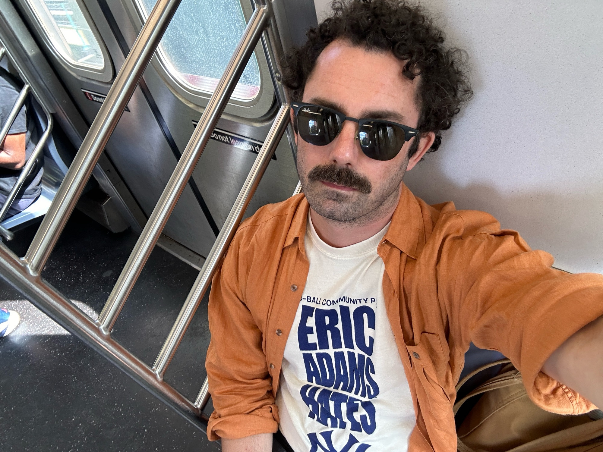 An image of a man on the subway with a t-shirt that reads “ERIC ADAMS HATES NY”