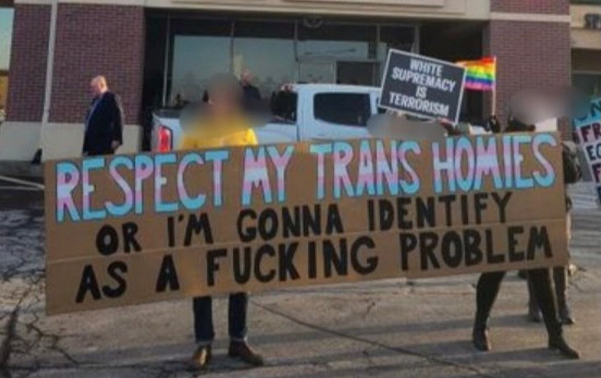 People holding a sign that says “respect my trans homies or I’m gonna identity as a fuckin problem”