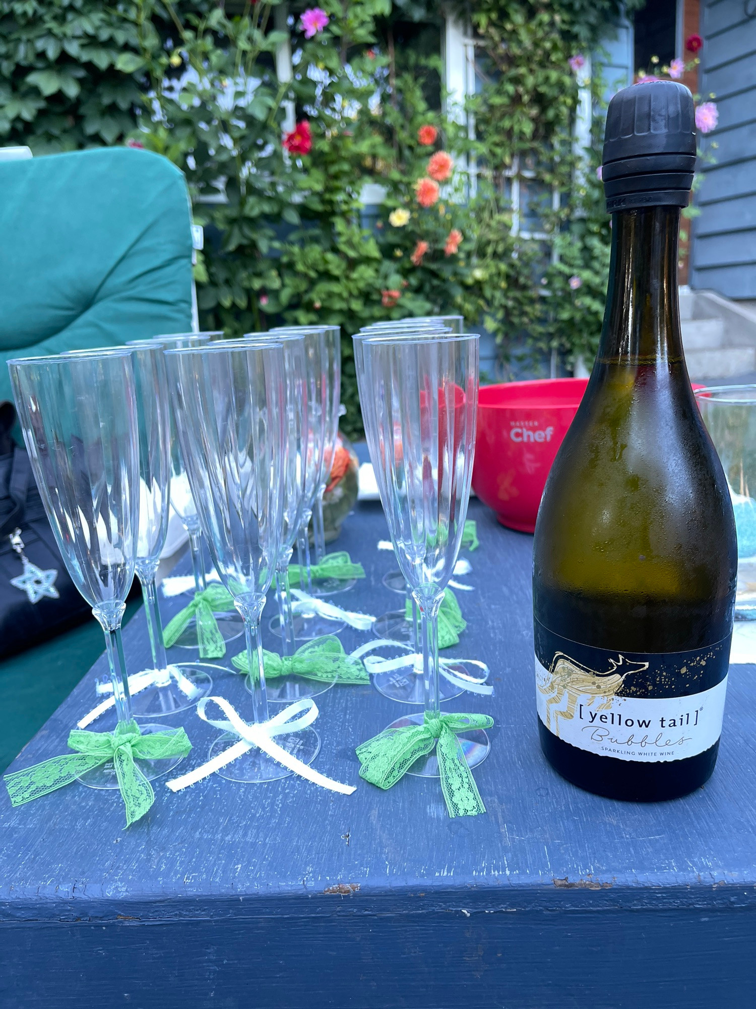 Champagne glasses with ribbon tied on them
Beside a bottle of bubbly and creeping flowers and ivy in the background