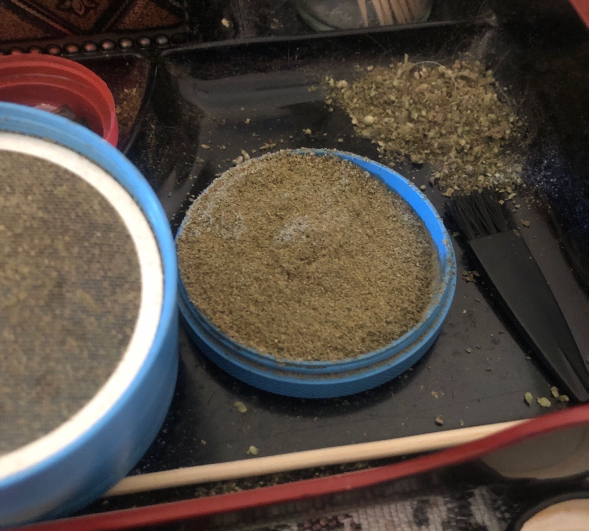 the kief catcher of a light blue weed grinder that is very full. it’s sitting next to a small pile of weed