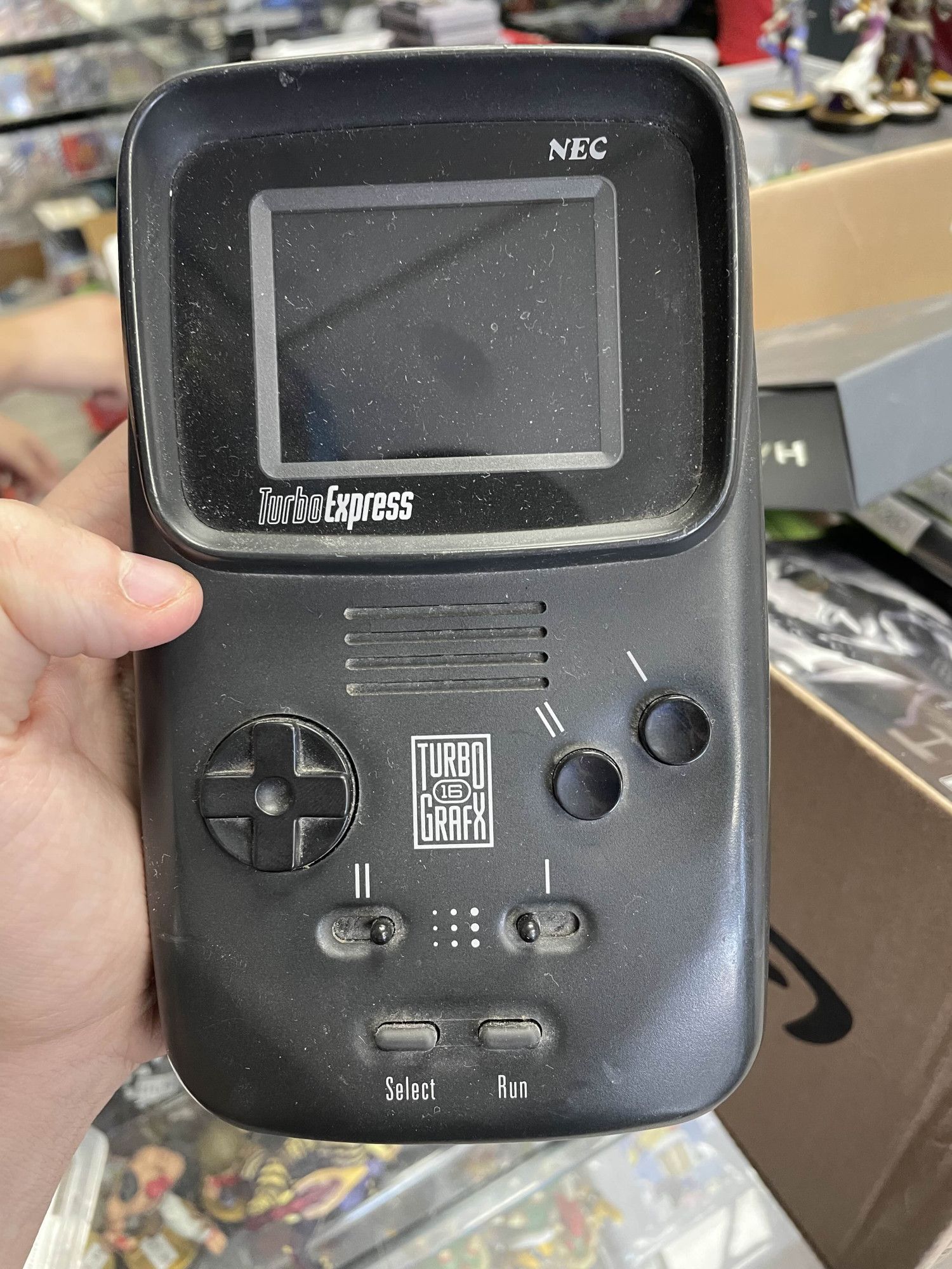 Me holding an NEC TurboExpress, a handheld version of the TurboGrafx-16 made in 1990. It features a color screen, 1 and 2 buttons labeled in roman numerals, turbo switches for said buttons, a d-pad, and "select" and "run" buttons.