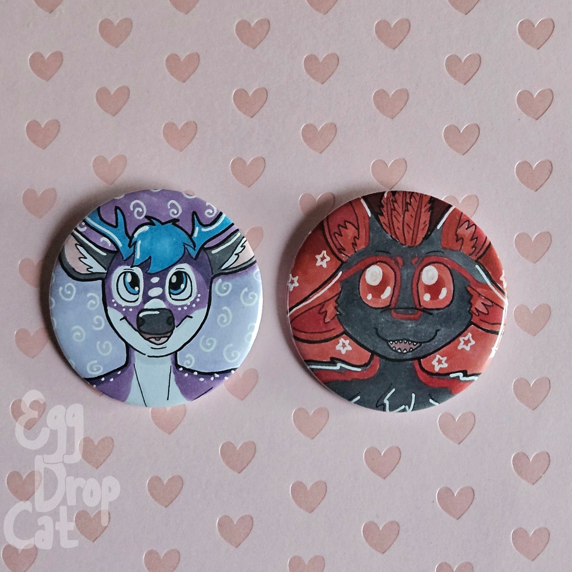 Two pin back buttons. One with a purple deer character, and one with a bird like character with black feathers and blue eyes