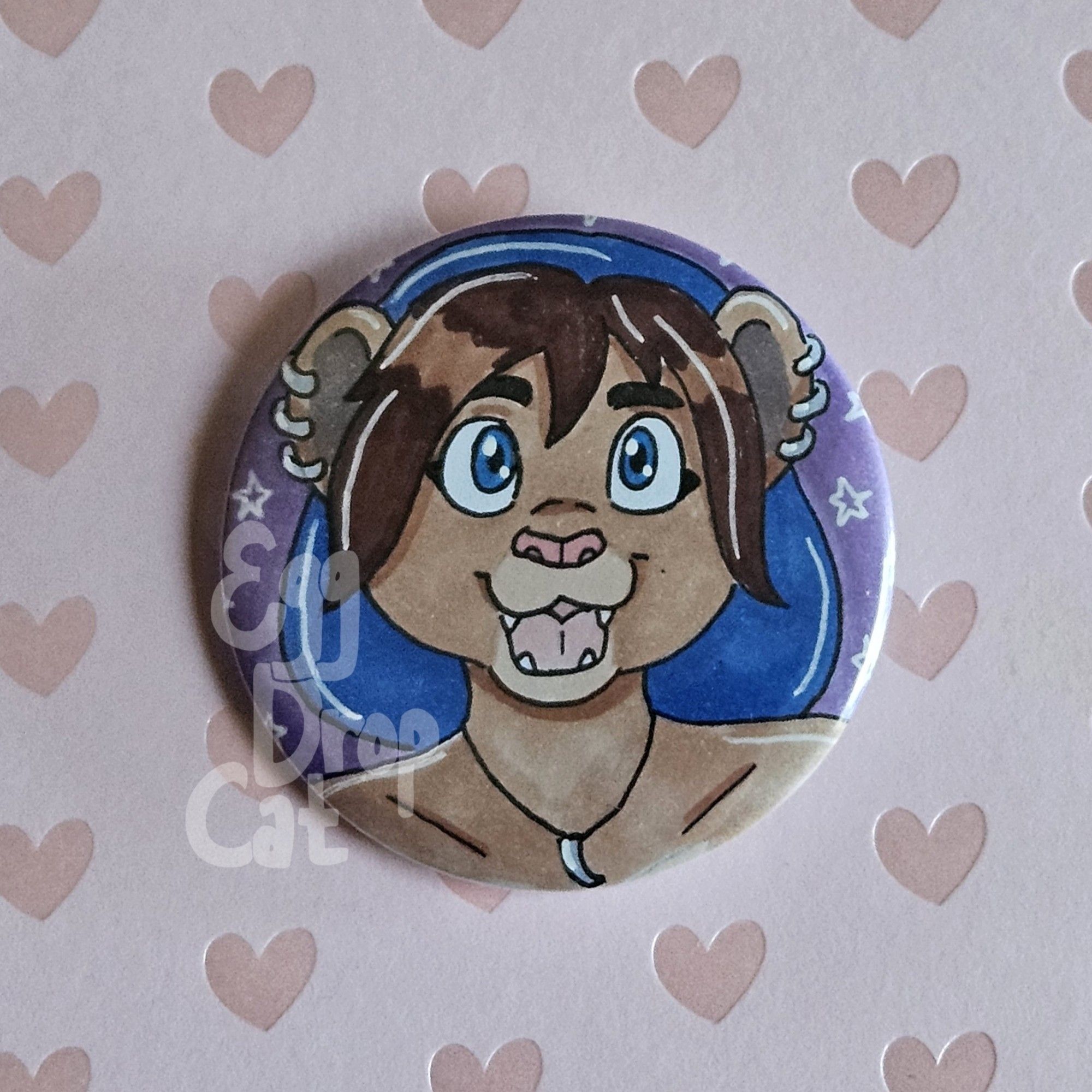 A button of a lion fursona with three earrings on each ear wearing a beanie