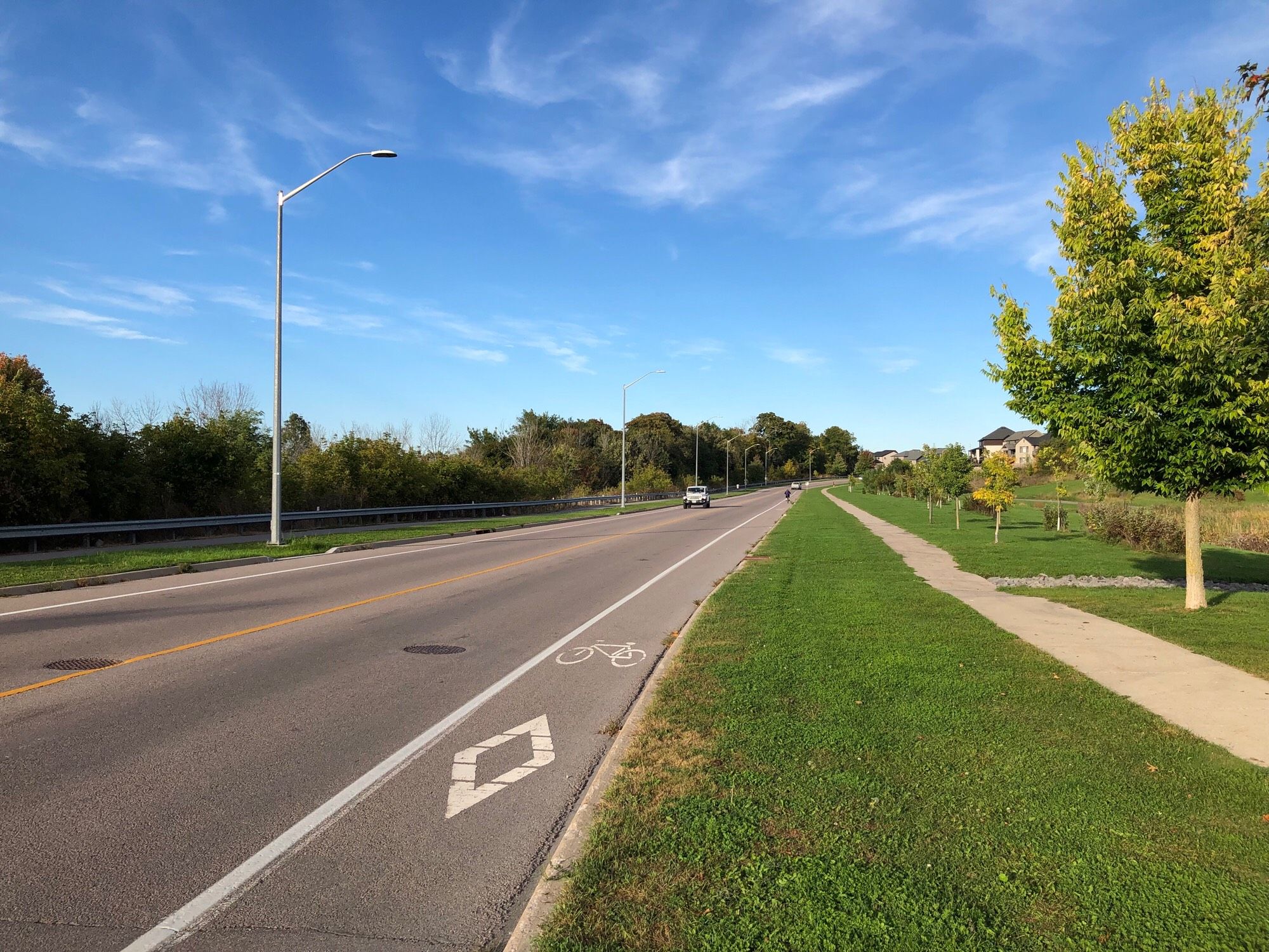 western start of Cataraqui Woods Drive, a residential semi-arterial street. The street has painted bike shoulders on both sides, which is the most common bike lane type in Kingston. In this case traffic typically tops out at 50kph so it’s not the worst.

There is also a concrete sidewalk on one side and multi-use path on the other. In the future a fully separated, AAA, bike lane could be built to replace the bike shoulders