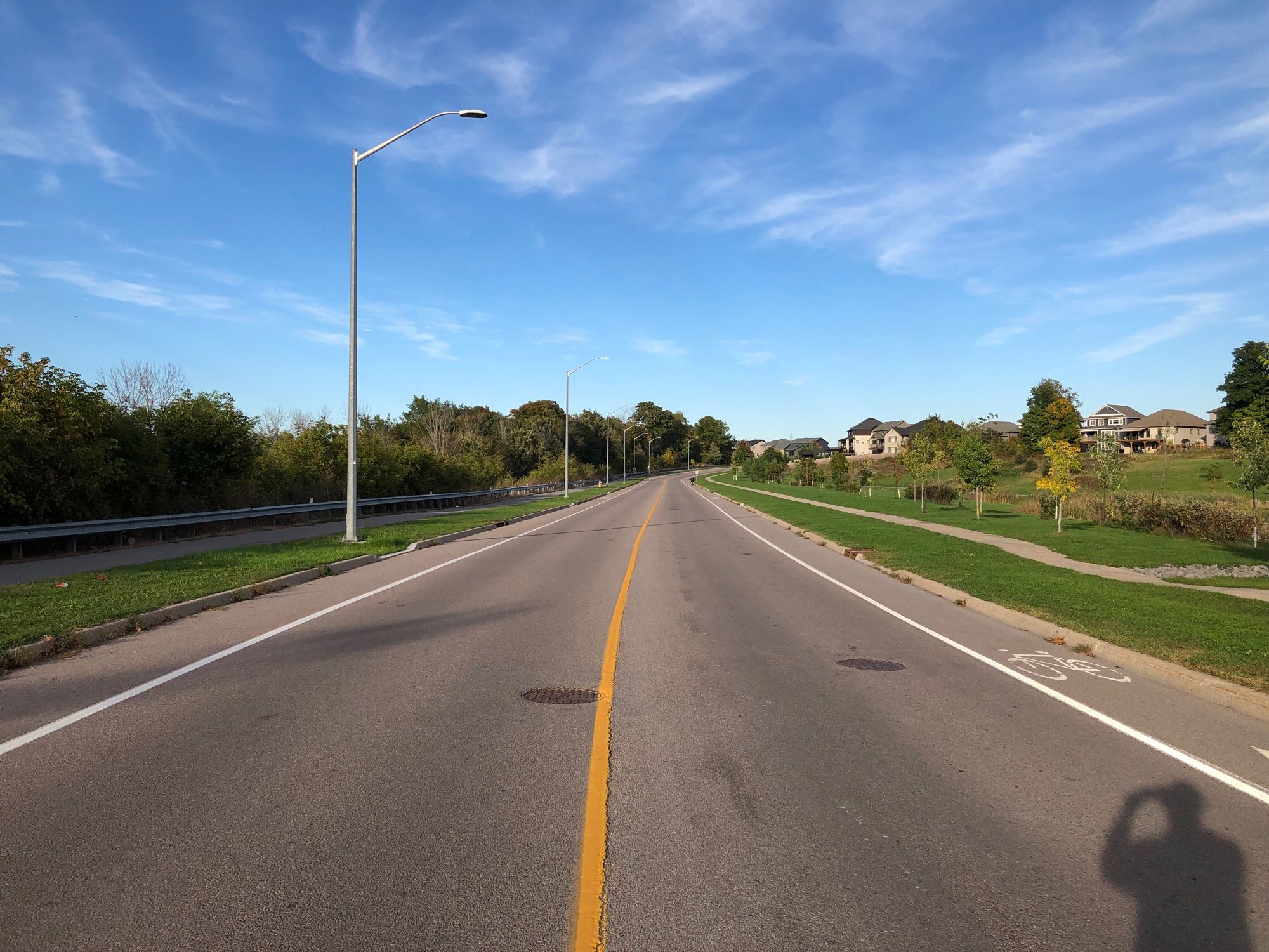 western start of Cataraqui Woods Drive, a residential semi-arterial street. The street has painted bike shoulders on both sides, which is the most common bike lane type in Kingston. In this case traffic typically tops out at 50kph so it’s not the worst.

There is also a concrete sidewalk on one side and multi-use path on the other. In the future a fully separated, AAA, bike lane could be built to replace the bike shoulders