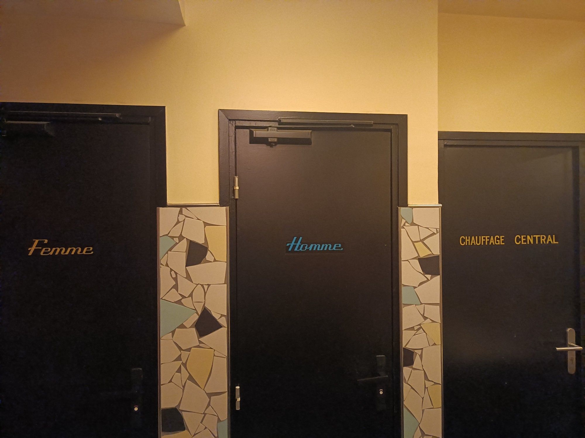 Une série de portes de toilettes indiquant "Femmes", "Hommes", et "Chauffage central"