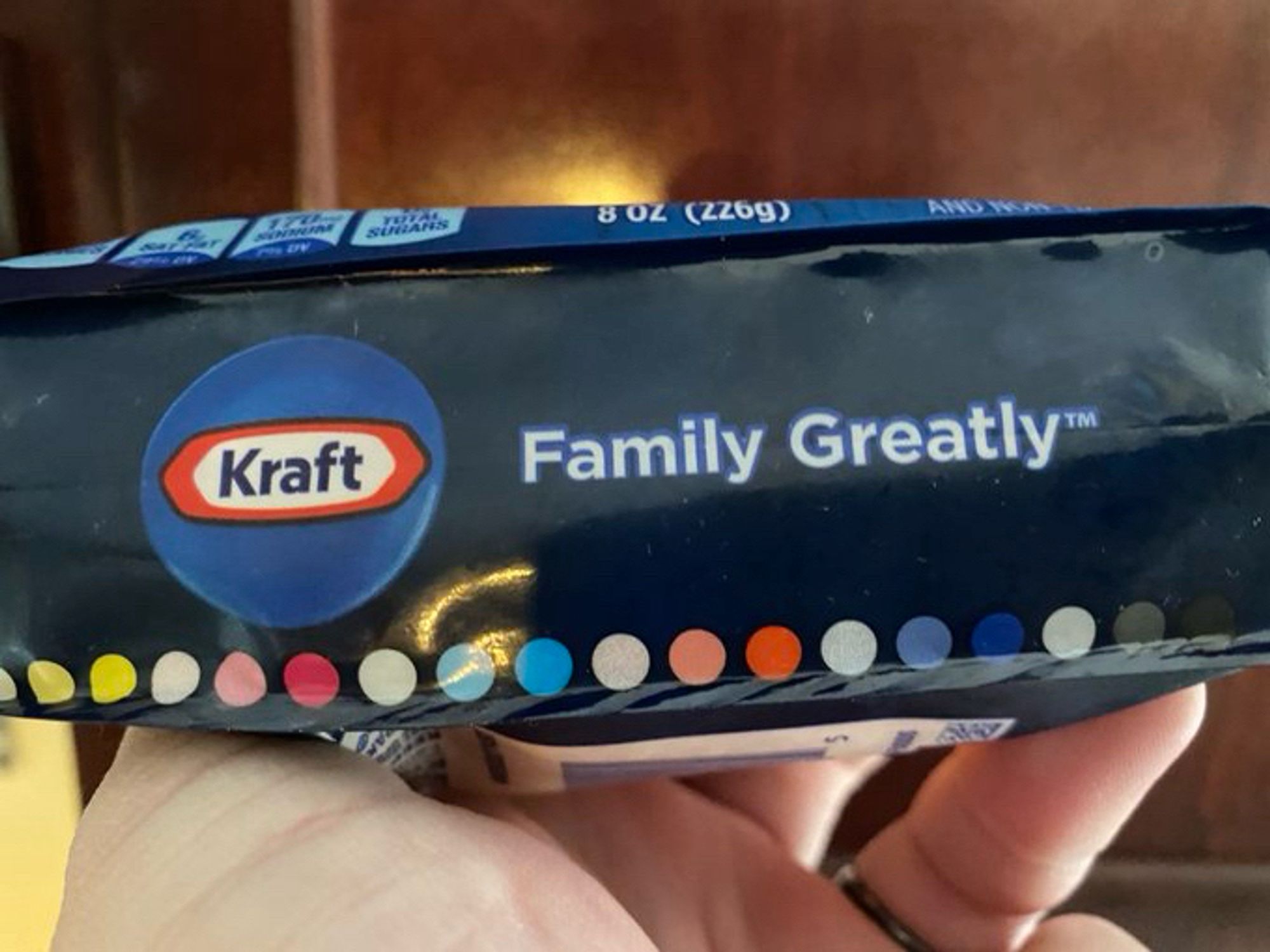 The bottom of a package of shredded cheese showing the Kraft logo — a thin white hexagonal shape with a red border and the name Kraft in dark blue text — and the slogan "Family Greatly™️."