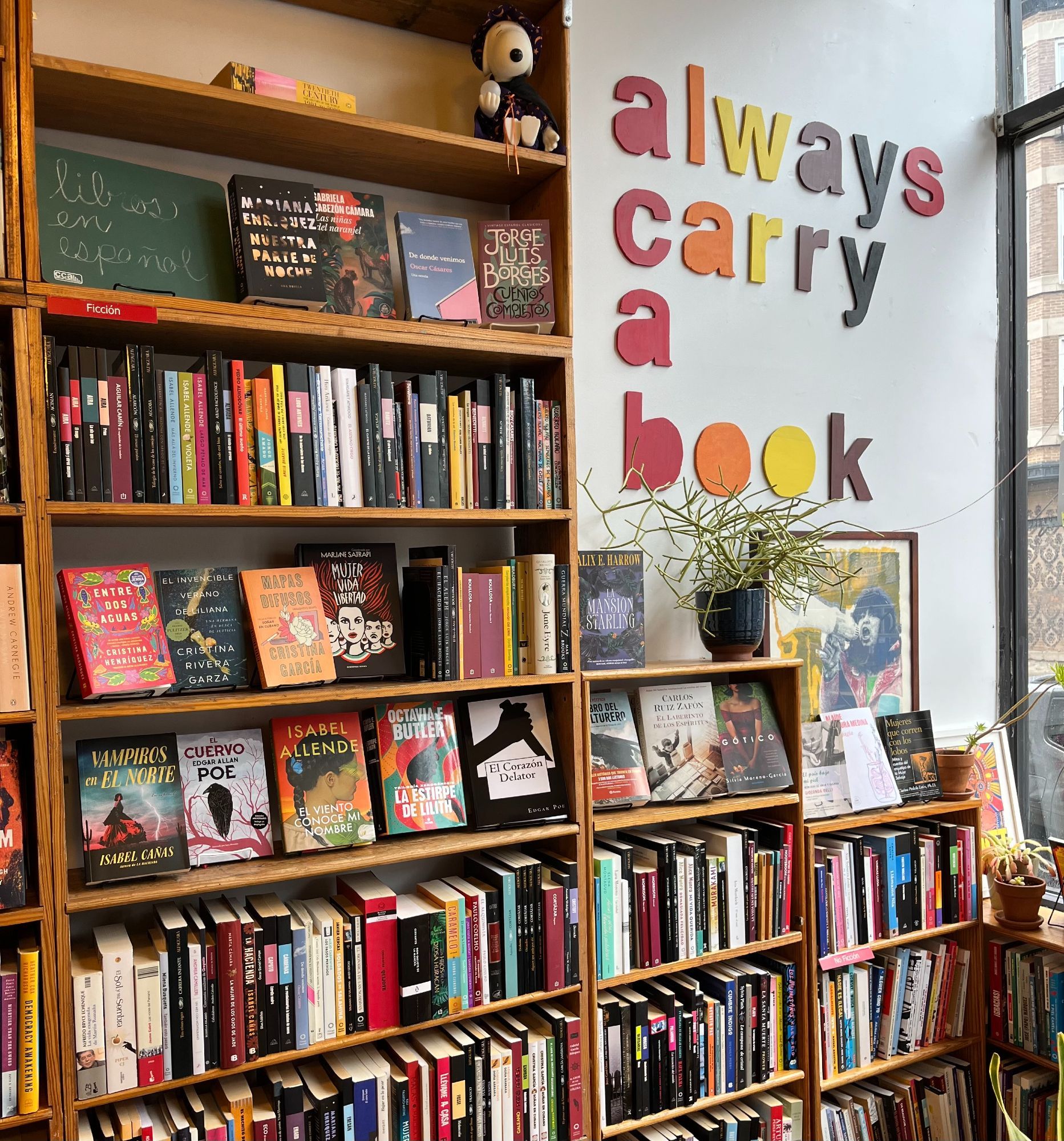 Floor to ceiling bookcases filled with books in spanish. Above one of the book cases are big multicolored letters that say "always carry a book". On the top right shelf sits a Snoopy doll.