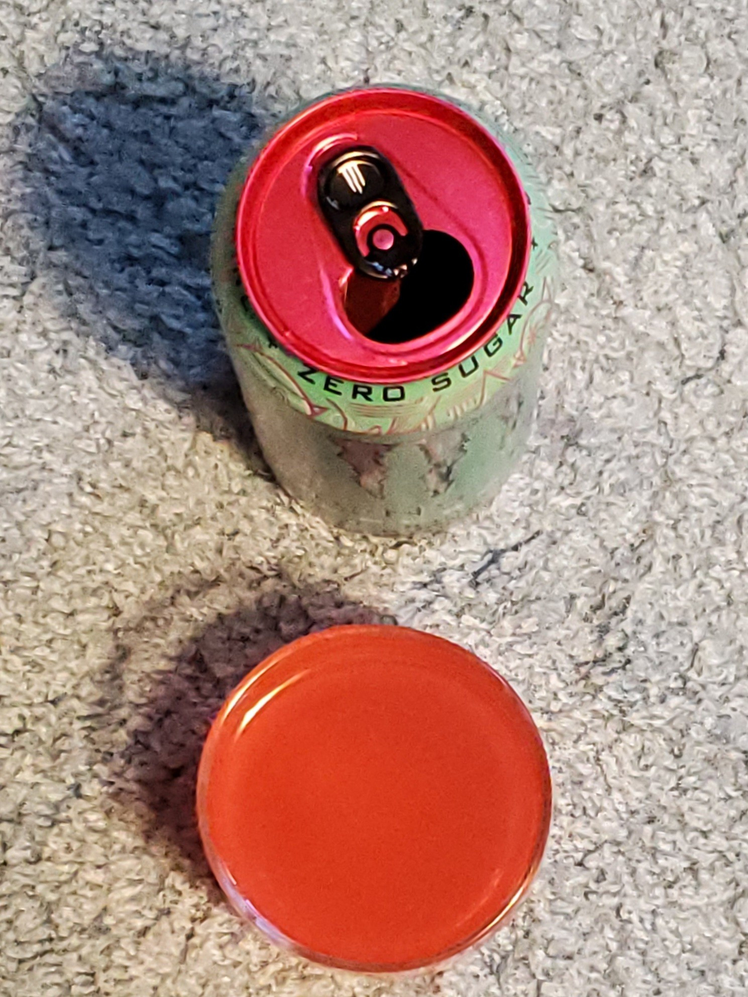 Top view of the same turquoise green Monster can with its pink top and black tab. The can is open. Of note on this shot is the shadow of the glass showing a small crescent of empty space between the rim and the liquid contents.