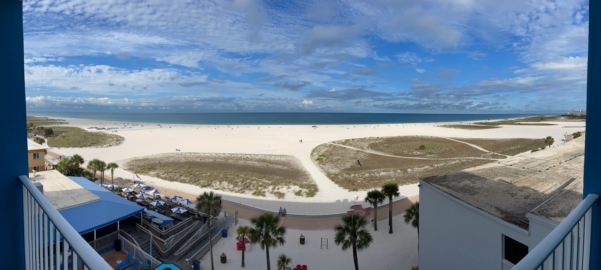 View from a balcony at a resort overlooking a beach with blue skies and some clouds.