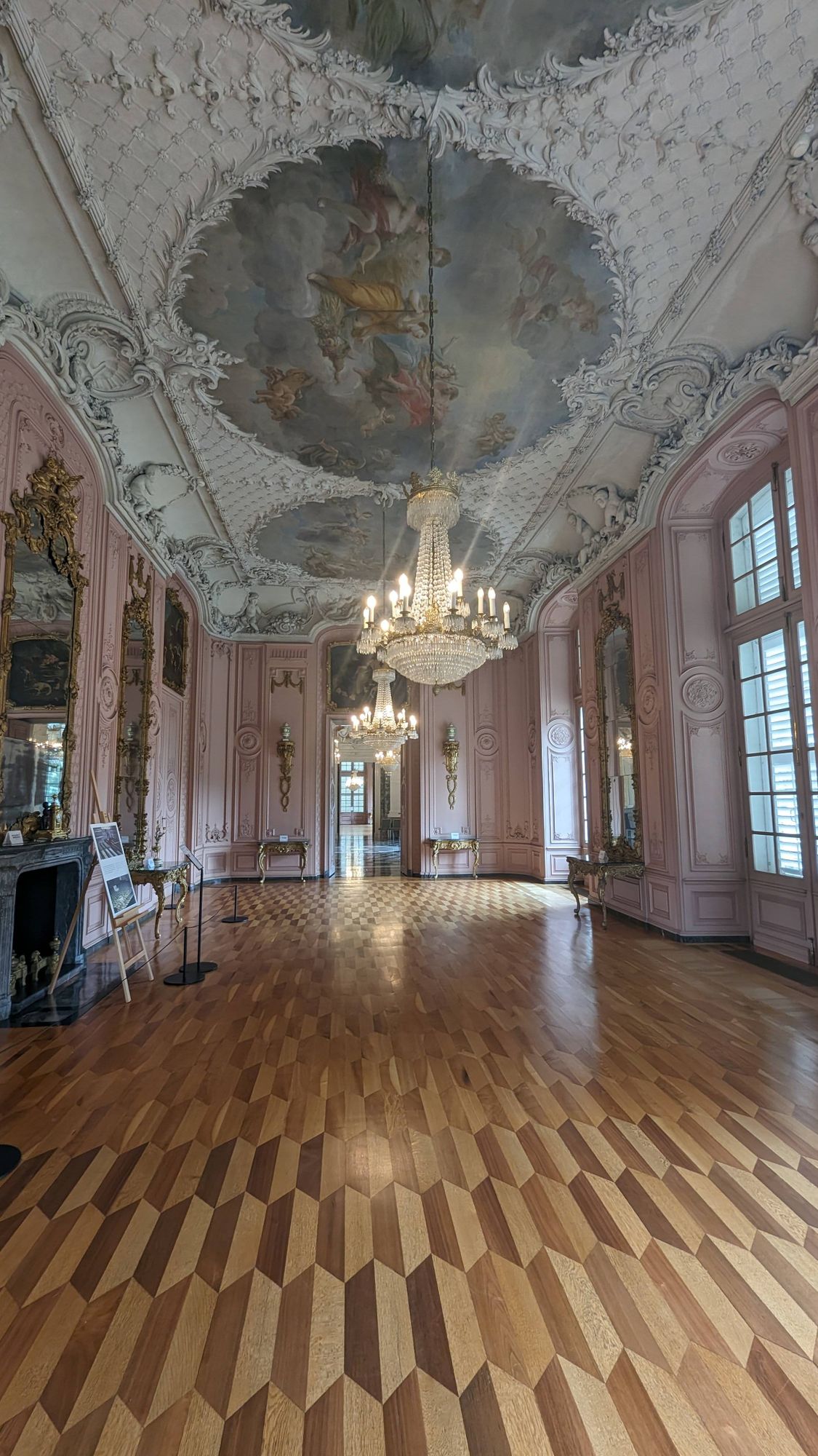 Pinker Saal mit Deckenfresko. Edelstes Parkett. Große Kronleuchter an der Decke.