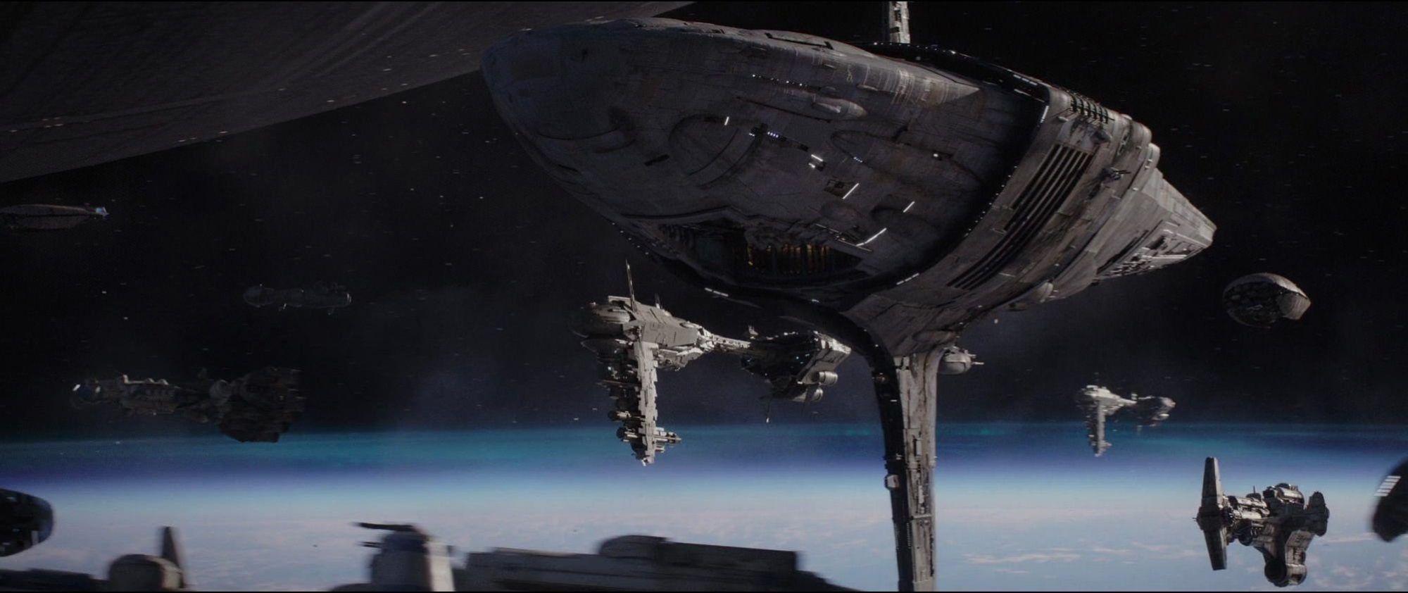 A shot from Rogue One: A Star Wars Story, showing a massive Rebel spaceship, the Profundity, hovering in orbit above the planet Scarif. Several smaller Rebels ships are flying around it.