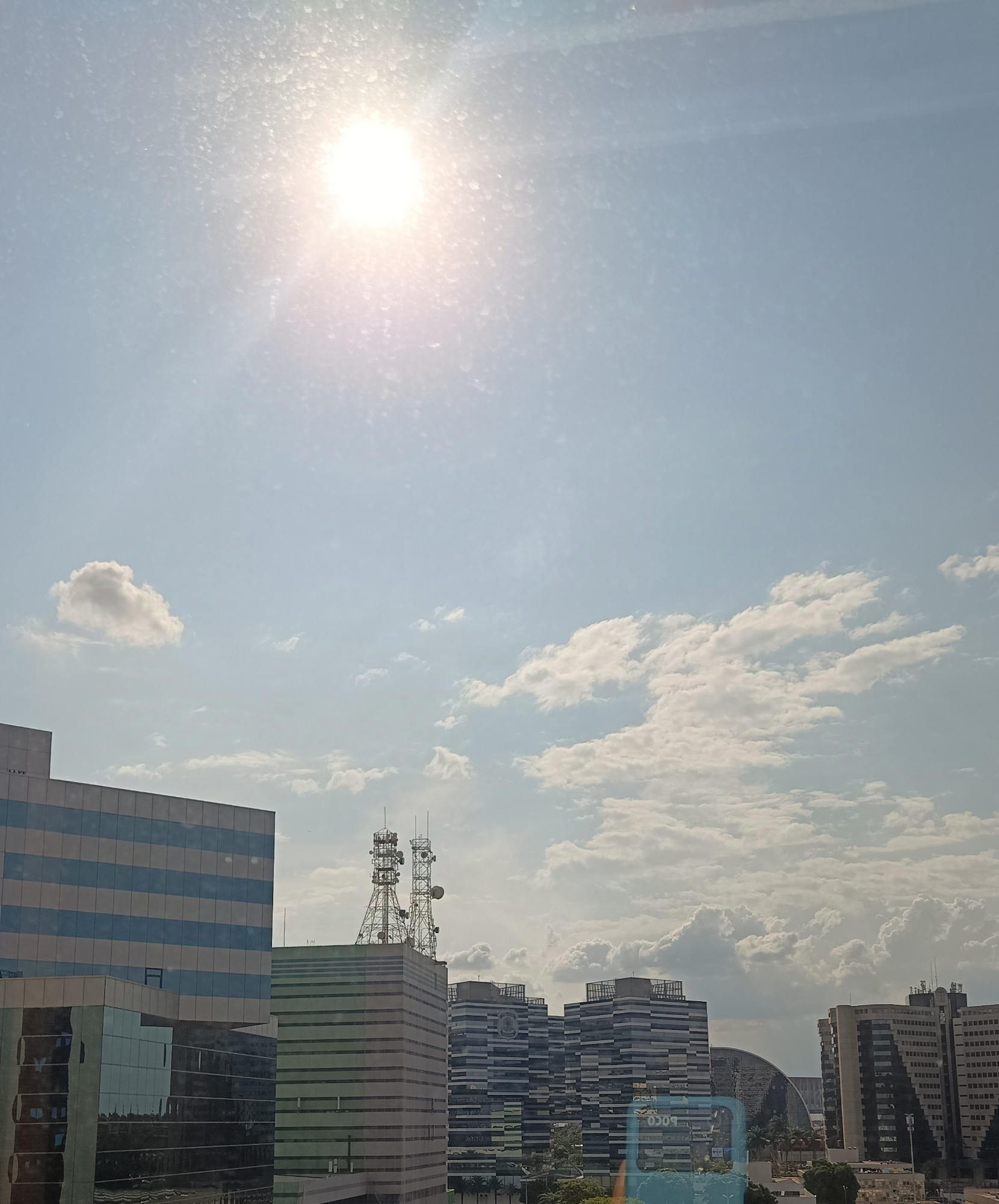 Foto de um céu azul e um baita sol, com prédios espelhados na parte inferior da foto