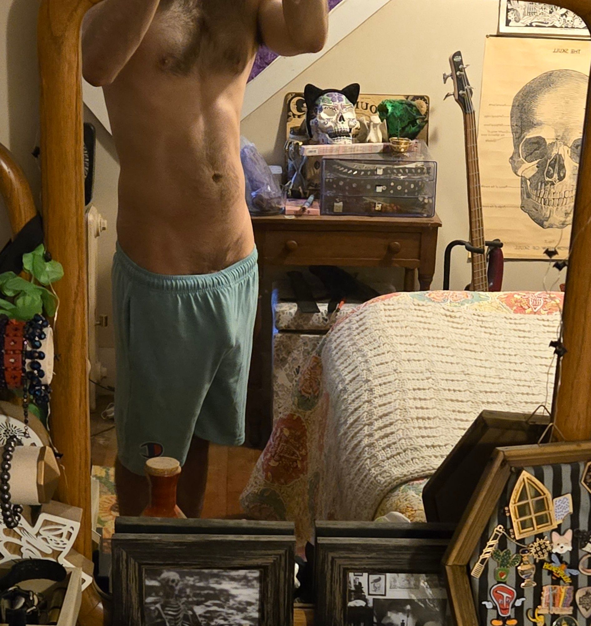 Mirror selfie of a human male in a cluttered room. He is wearing turquoise gym shorts that ride low and cling to the outline of his mostly limp penis.