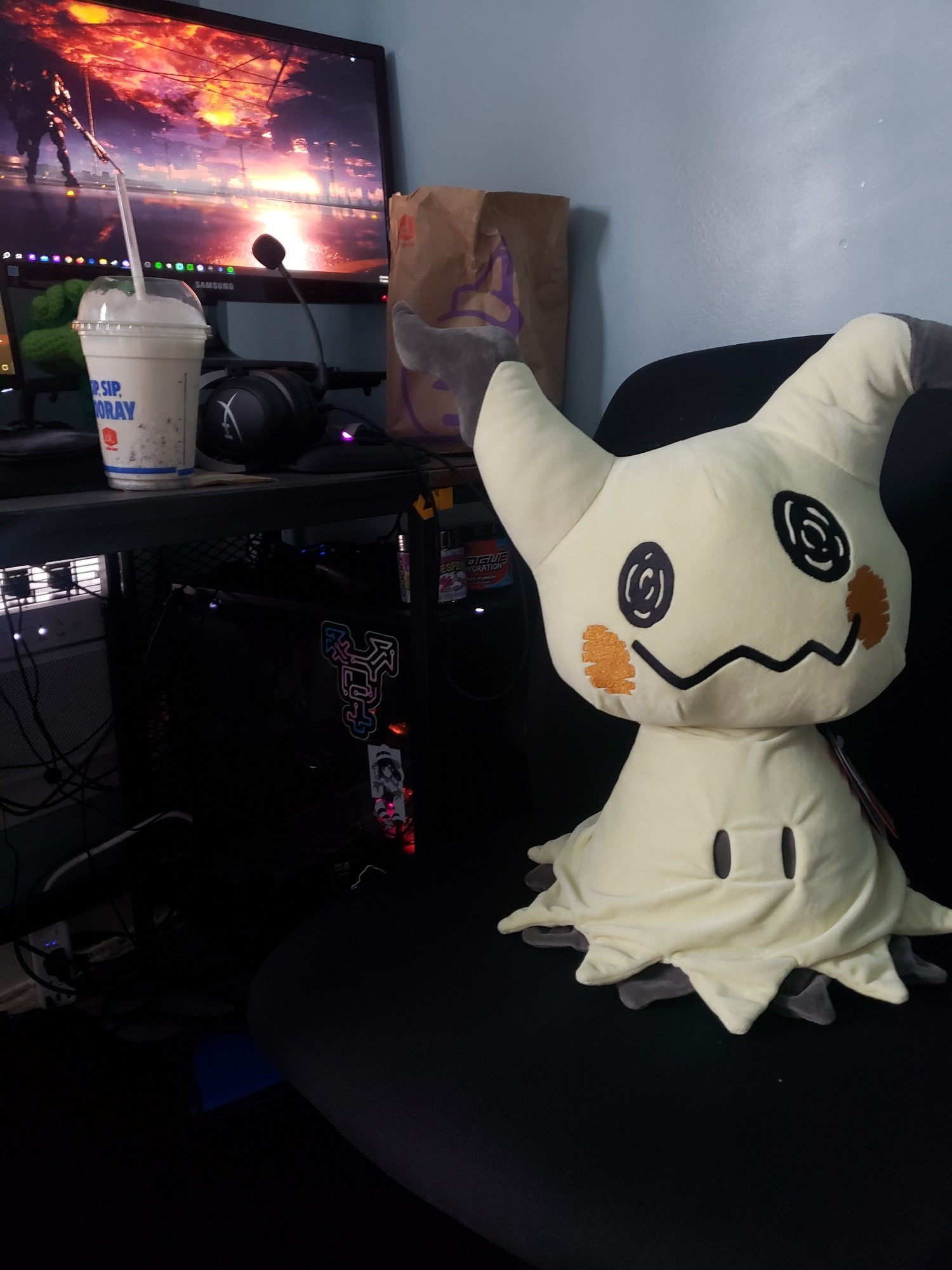 A life size mimikyu plushie sat in Xili's chair, next to a milkshake. The weeks nonsense budget already spent.