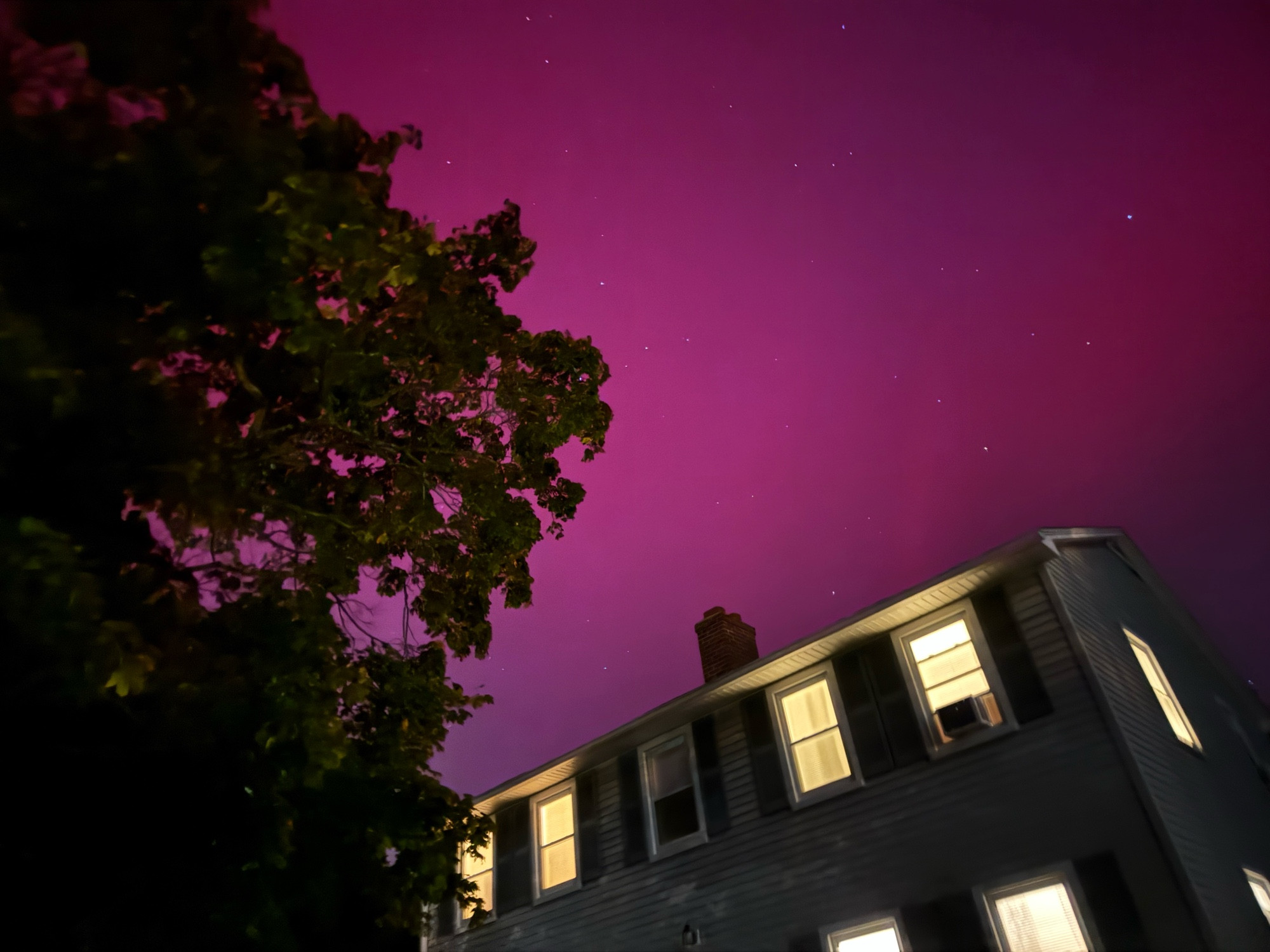 Norther lights in the sky with a view of a house and part of a tree.