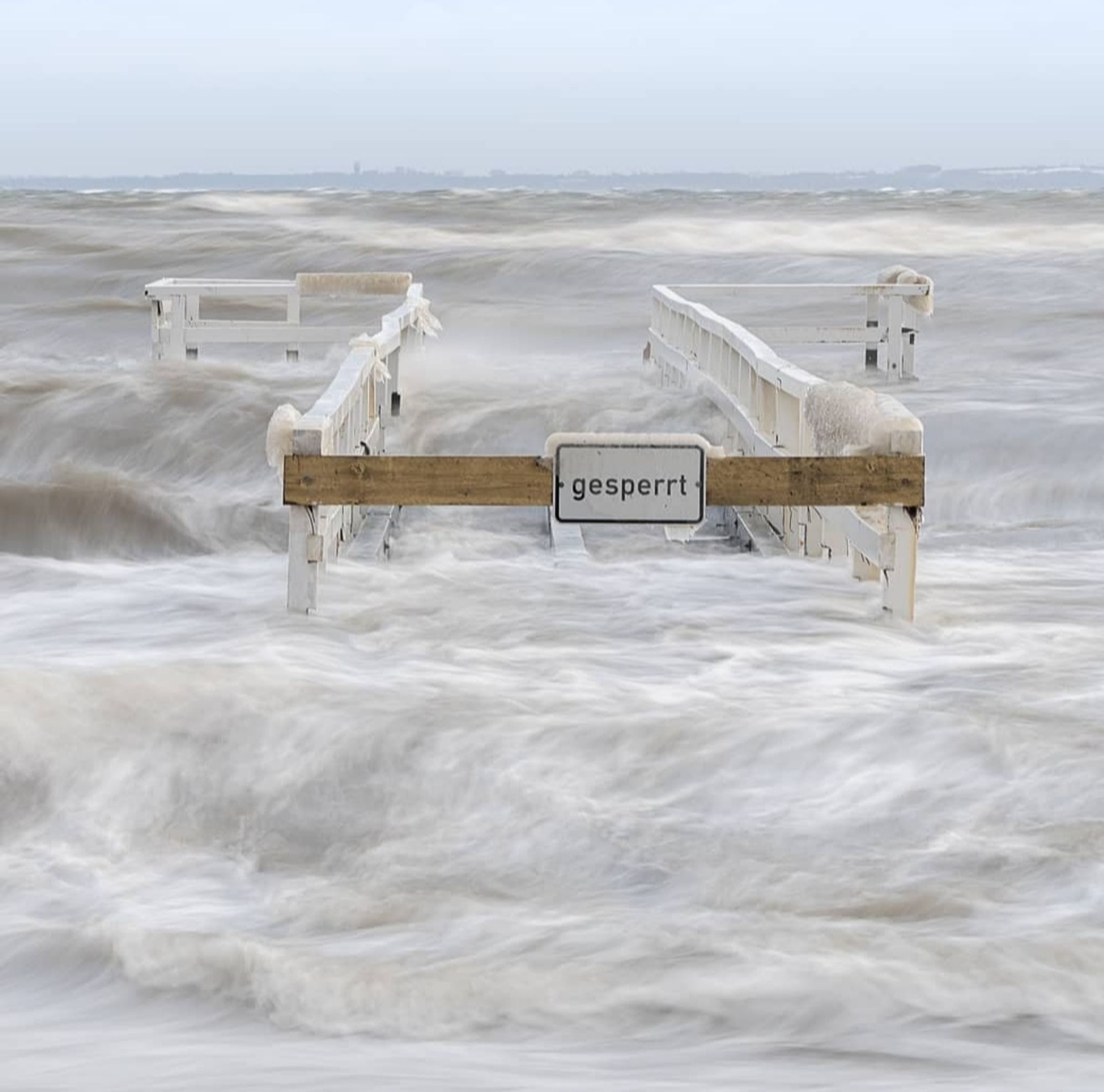 Wintersturm an der Ostsee. Die Geländer einer kleinen Seebrücke ragen noch aus dem Wasser.