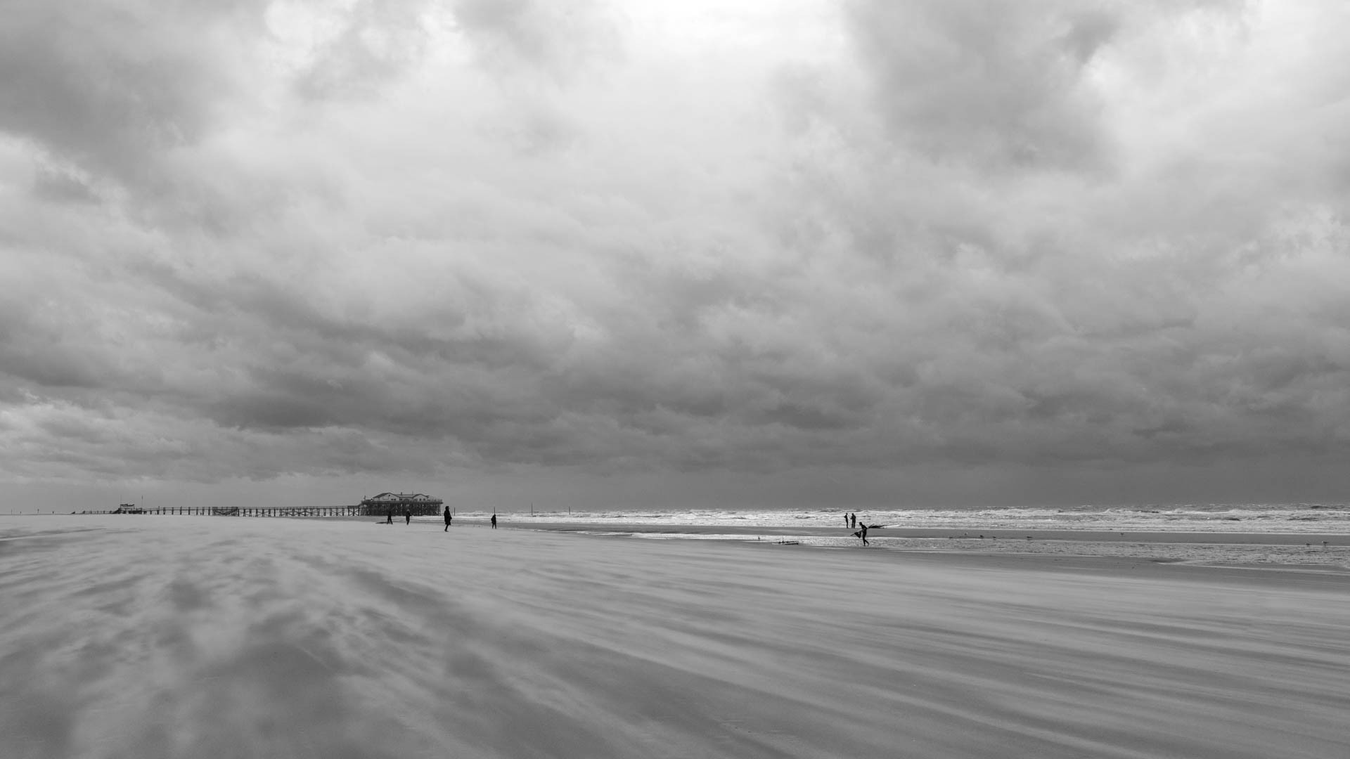 Bedrohlicher Wolkenhimmel über einem Strand, über den der Sand getrieben wird. 