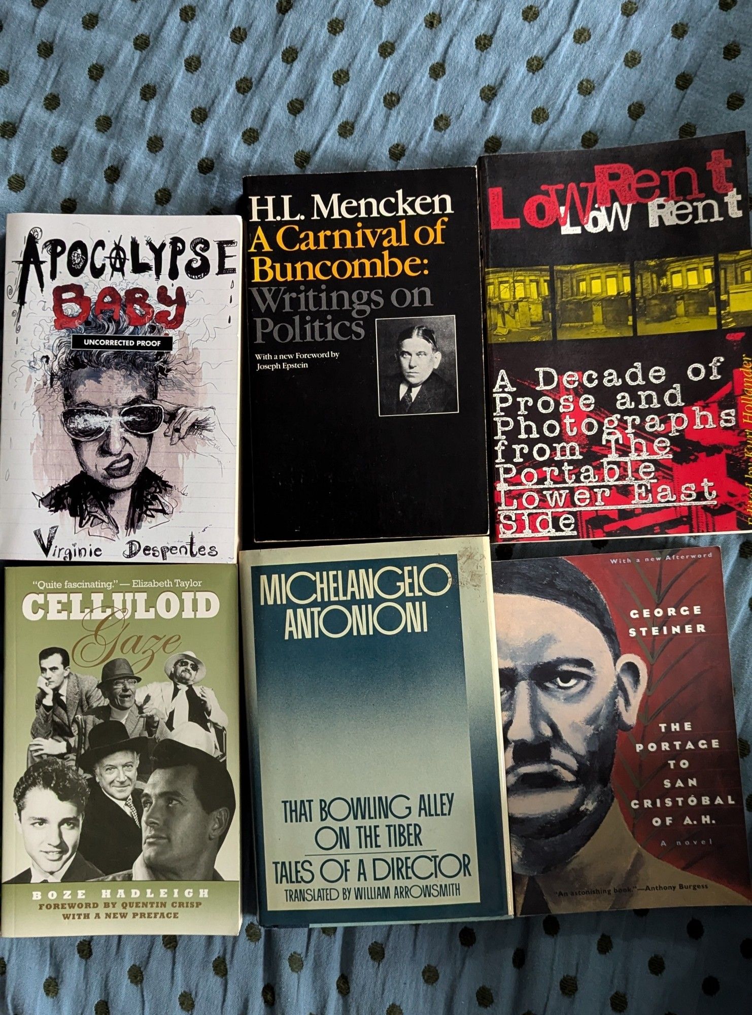 six books displayed on a blue bedspread 
Virginie Despentes: Apocalypse Baby
H.L. Mencken: A Carnival of Buncombe 
Low Rent - A Decade of Prose and Photographs from "The Portable Lower East Side"
Boze Hadleigh: Celluloid Gaze
Michelangelo Antonioni: That Bowling Alley On The Tiber
George Steiner: The Portage To San Cristobal of A. H.