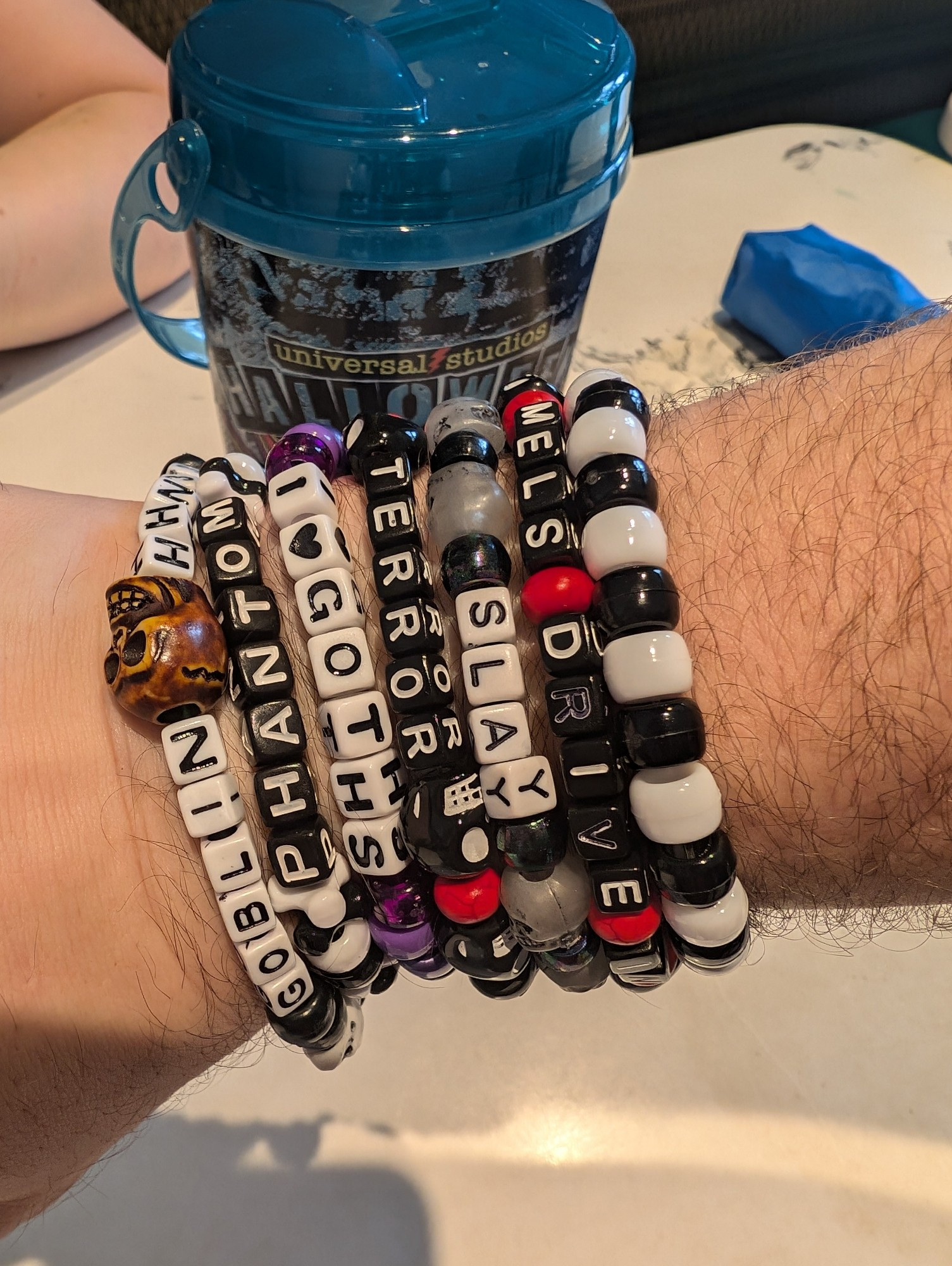 Image shows my wrist with several beaded bracelets, with Halloween themes and sayings such as "Slay", "Terror", and "I Love Goths". Most of the bracelets have skull shaped beads on them.