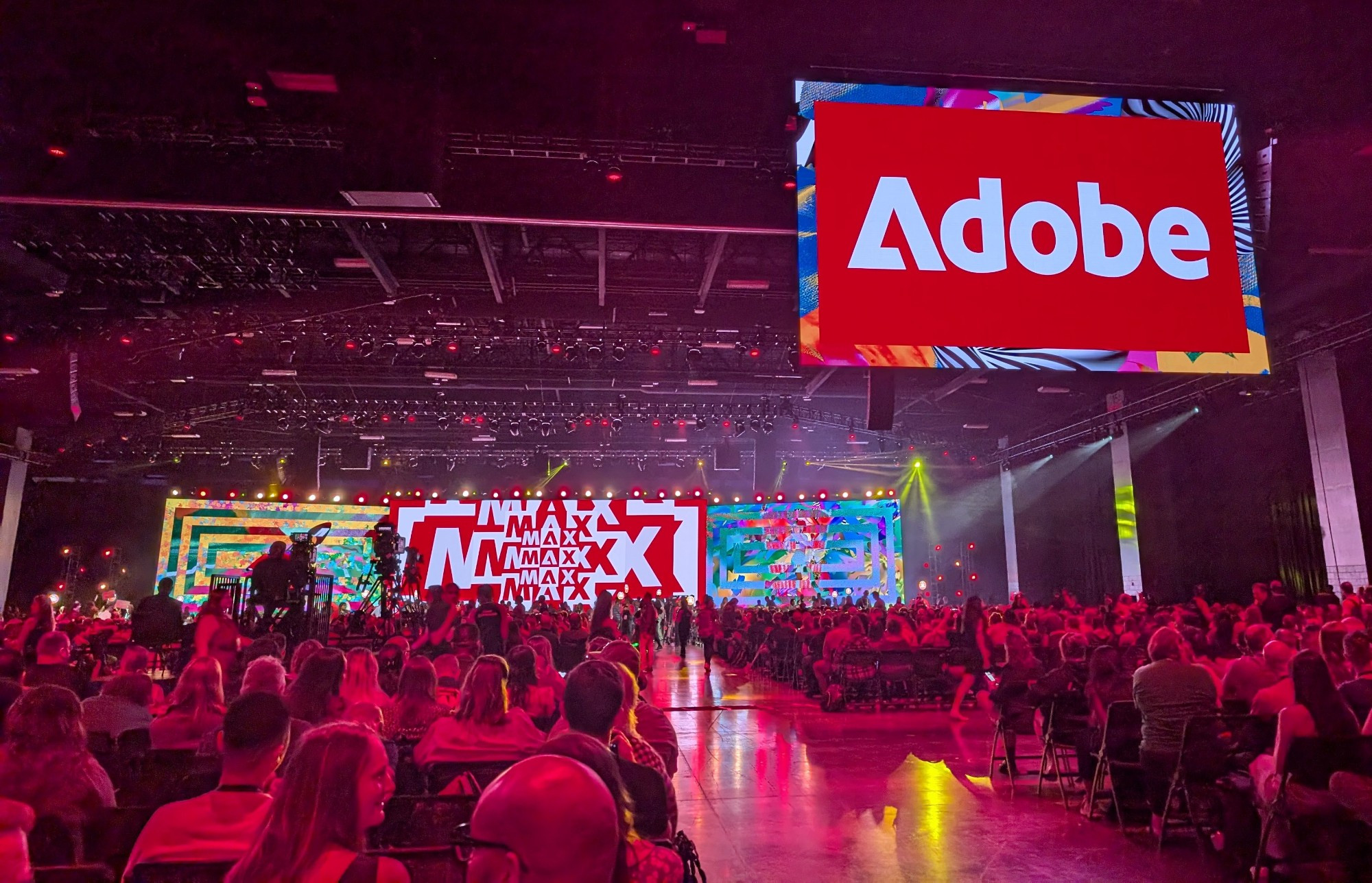 A large room with people sitting in chairs waiting for the keynote opening speeches to start. Giants screens say Adobe and Max.