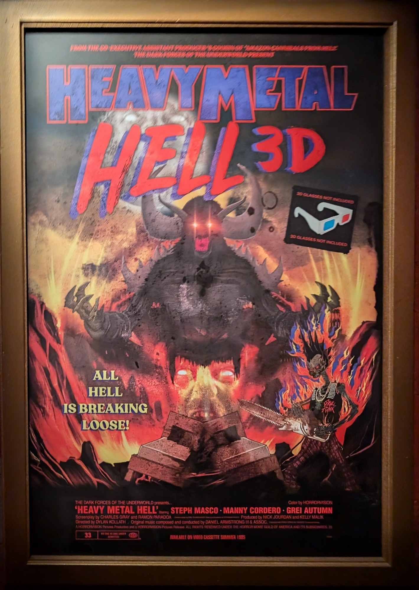 Poster for a fake movie called Heavy Metal Hell 3D. Featuring the image of a black demon with his arms outstretched and a skeleton with a Mohawk and a chainsaw. There is a tagline that says "All hell is breaking loose."