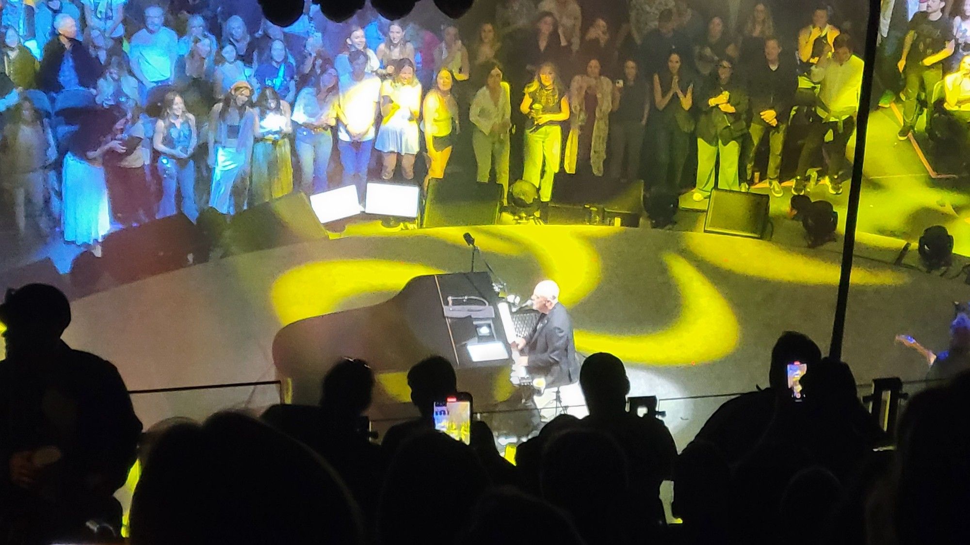 Billy Joel on stage at his piano bathed in golden light.