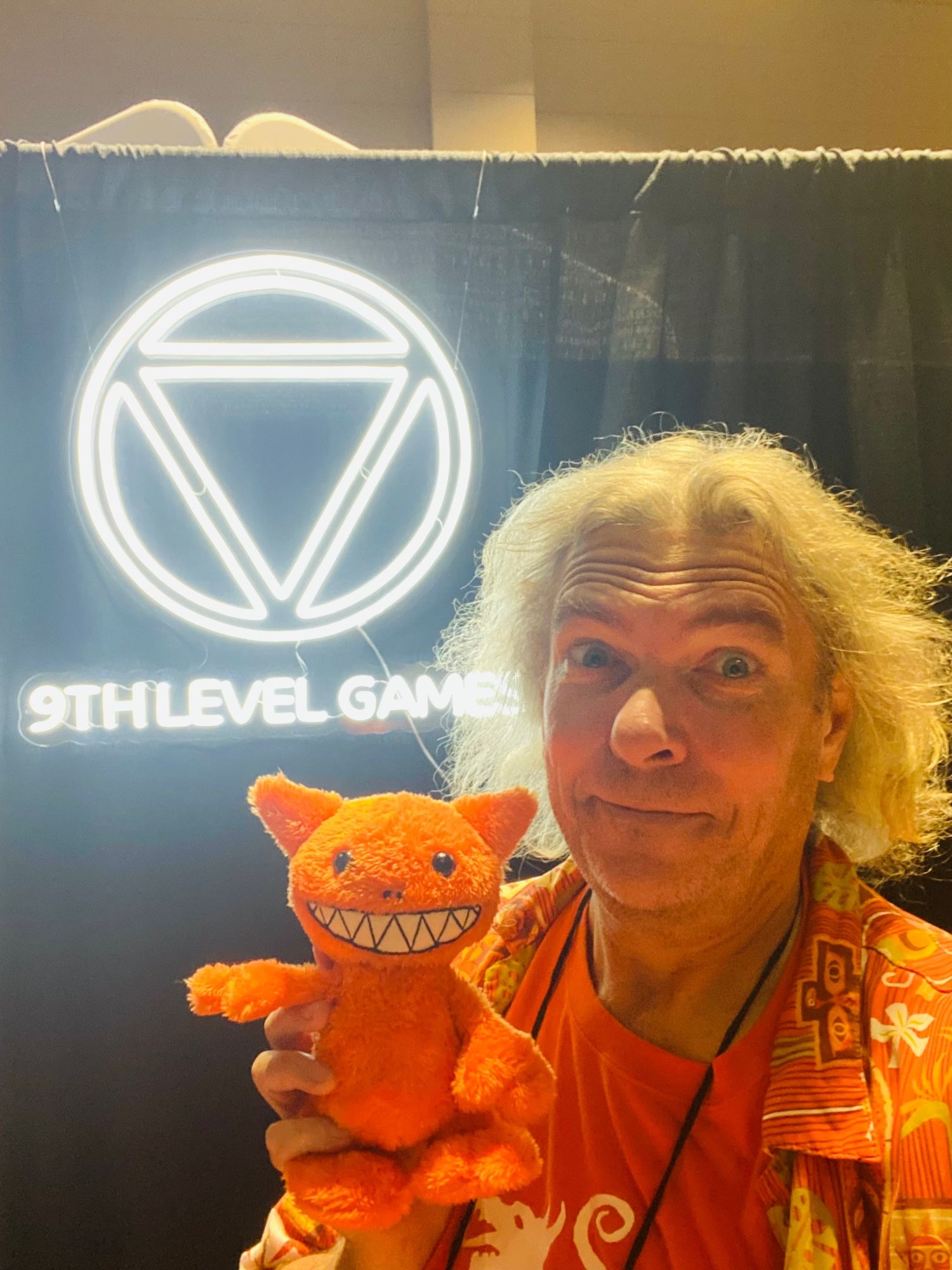 An old fool in Hawaiian shirt at the 9th Level Games booth. He’s posing with a small, but ferocious, plush Kolbold.