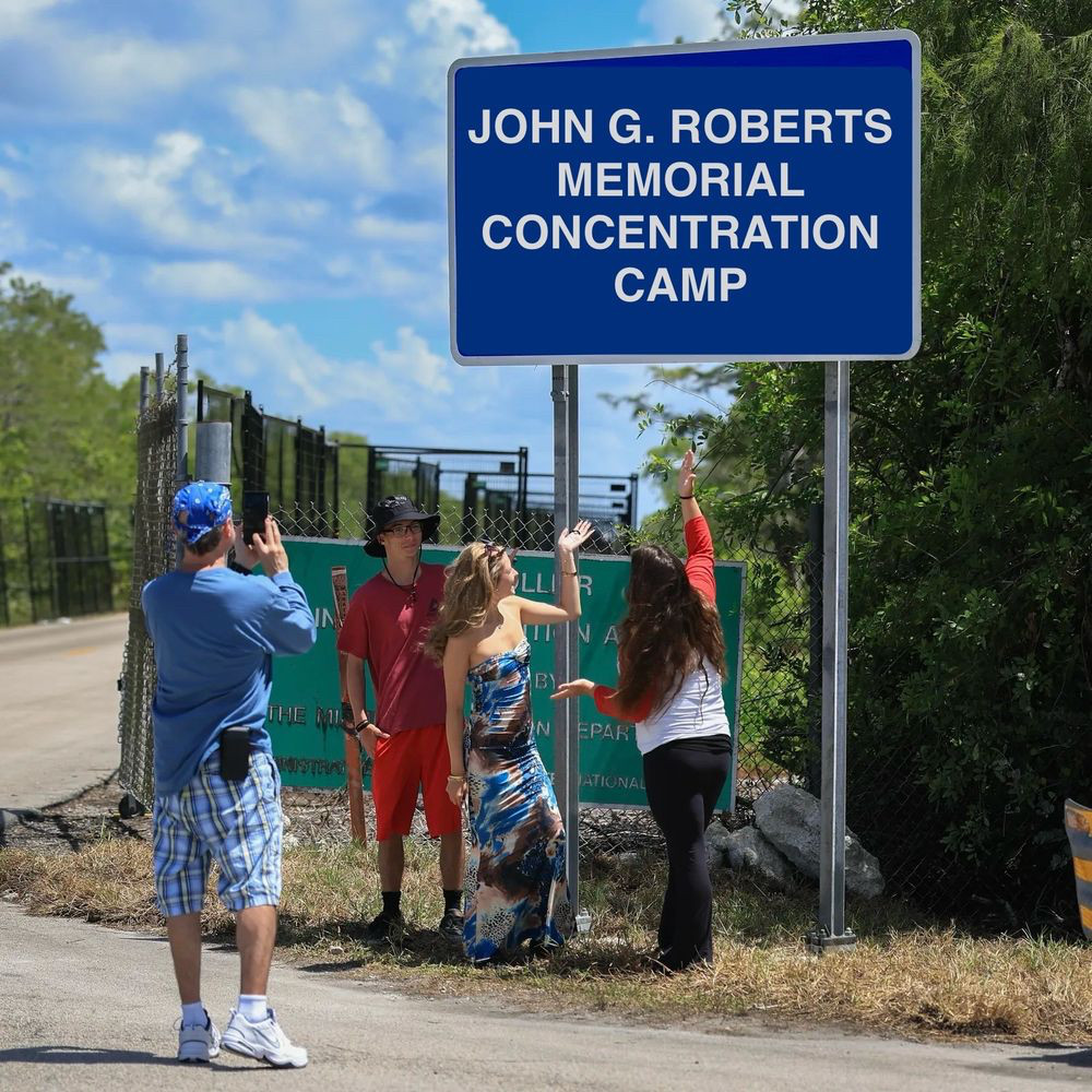 Tourists taking a selfie in front of a large highway sign: 
JOHN G. ROBERTS
MEMORIAL
CONCENTRATION
CAMP
